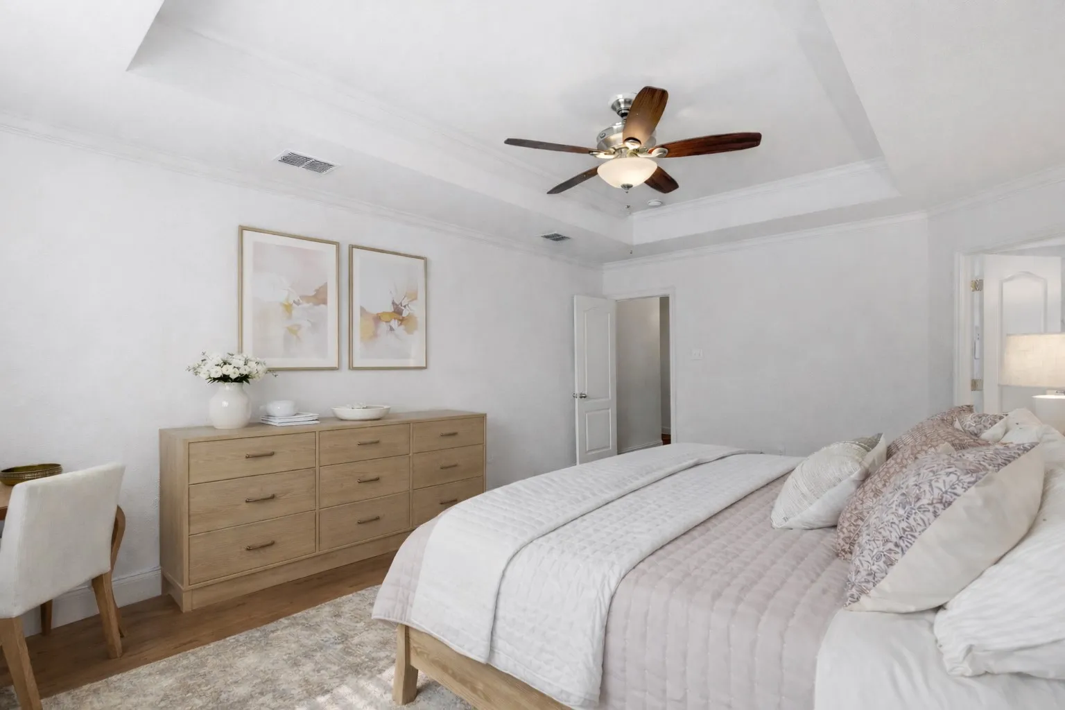 This bedroom features a tray ceiling with a ceiling fan, hardwood flooring, and light-colored walls