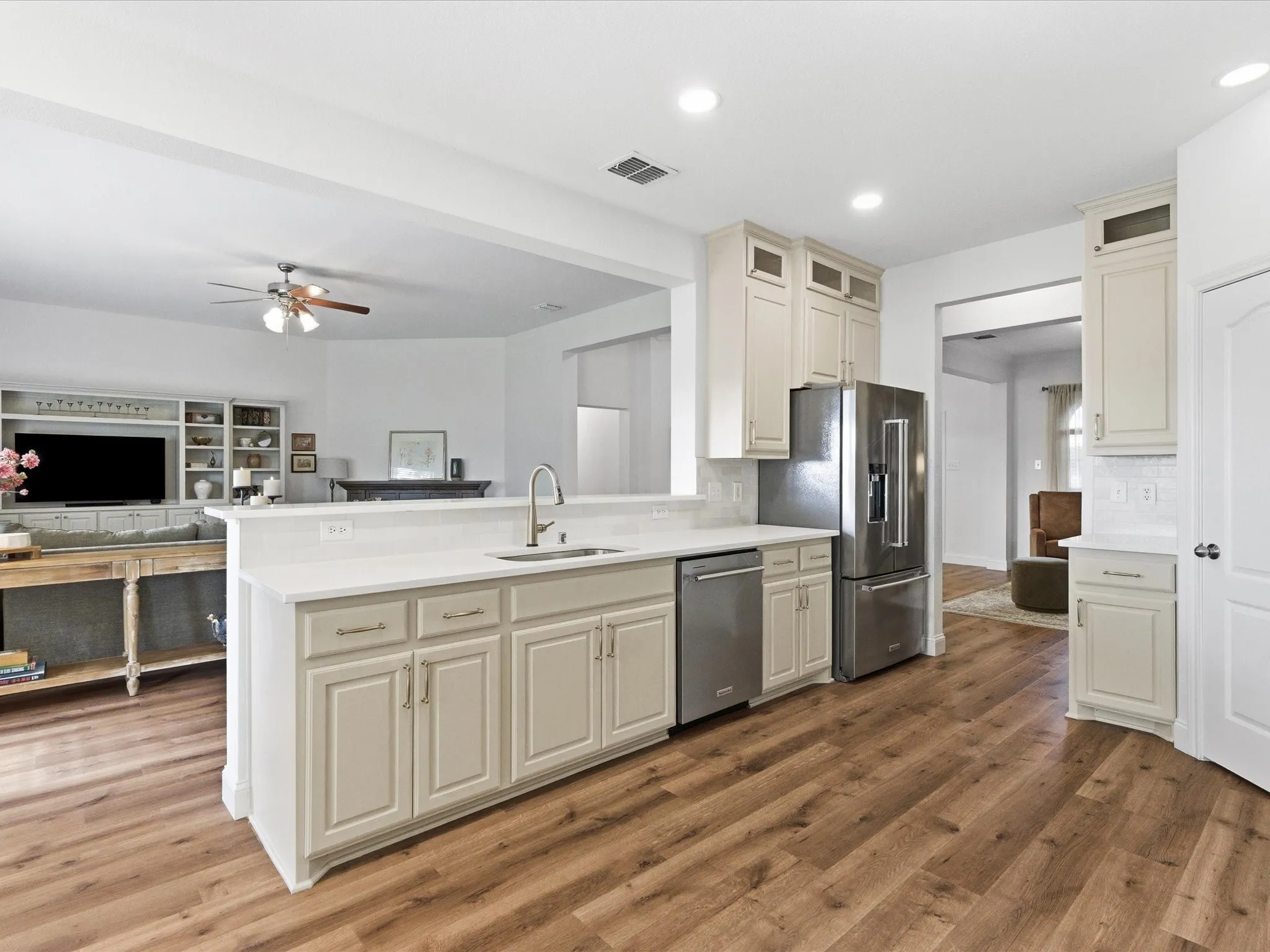 The kitchen features wood-look flooring, light-colored cabinetry, stainless steel appliances, and a kitchen island with a sink and white countertop