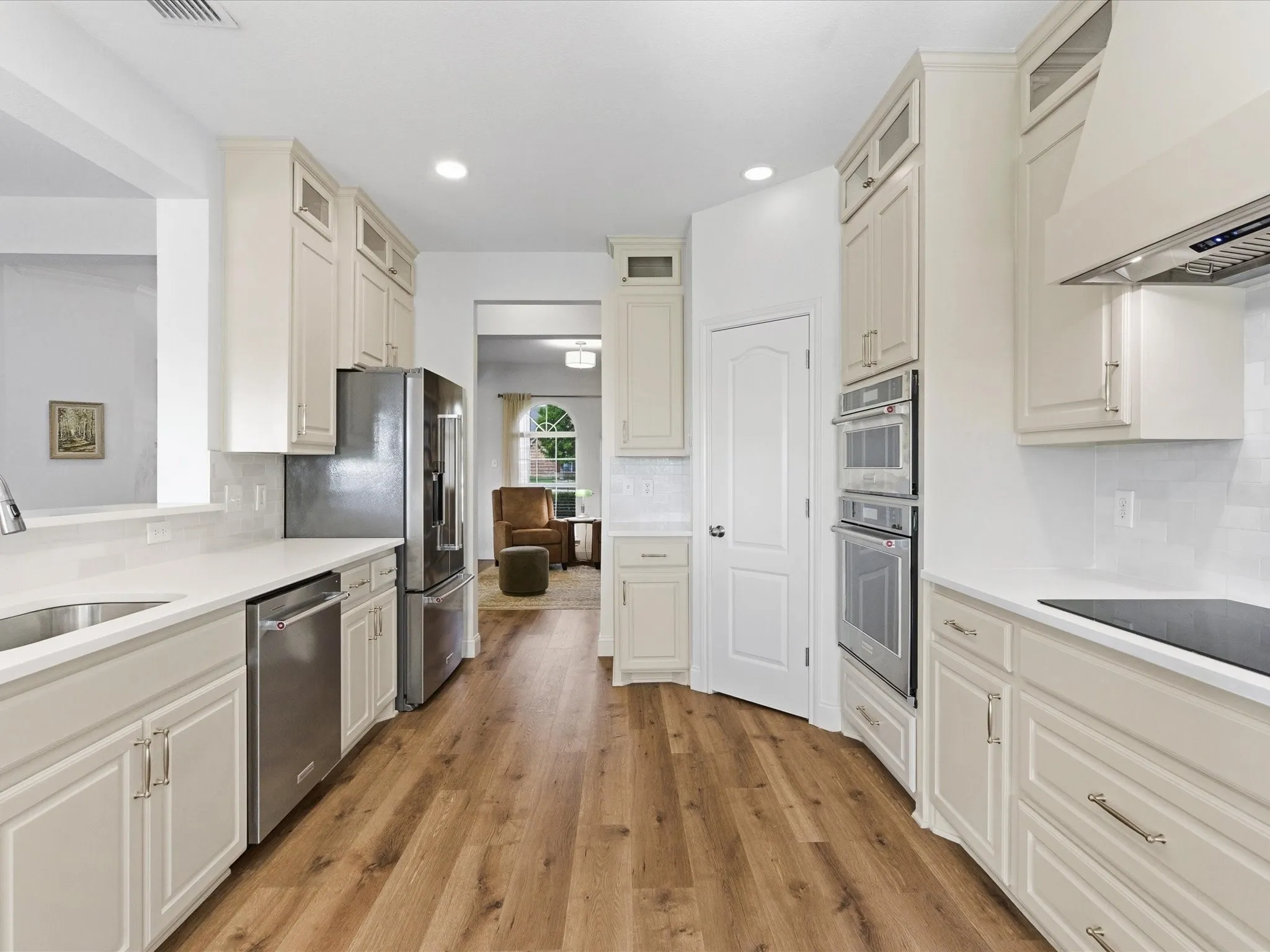 This kitchen features light-colored cabinetry, stainless steel appliances including a refrigerator, dishwasher, and double oven, and a built-in cooktop