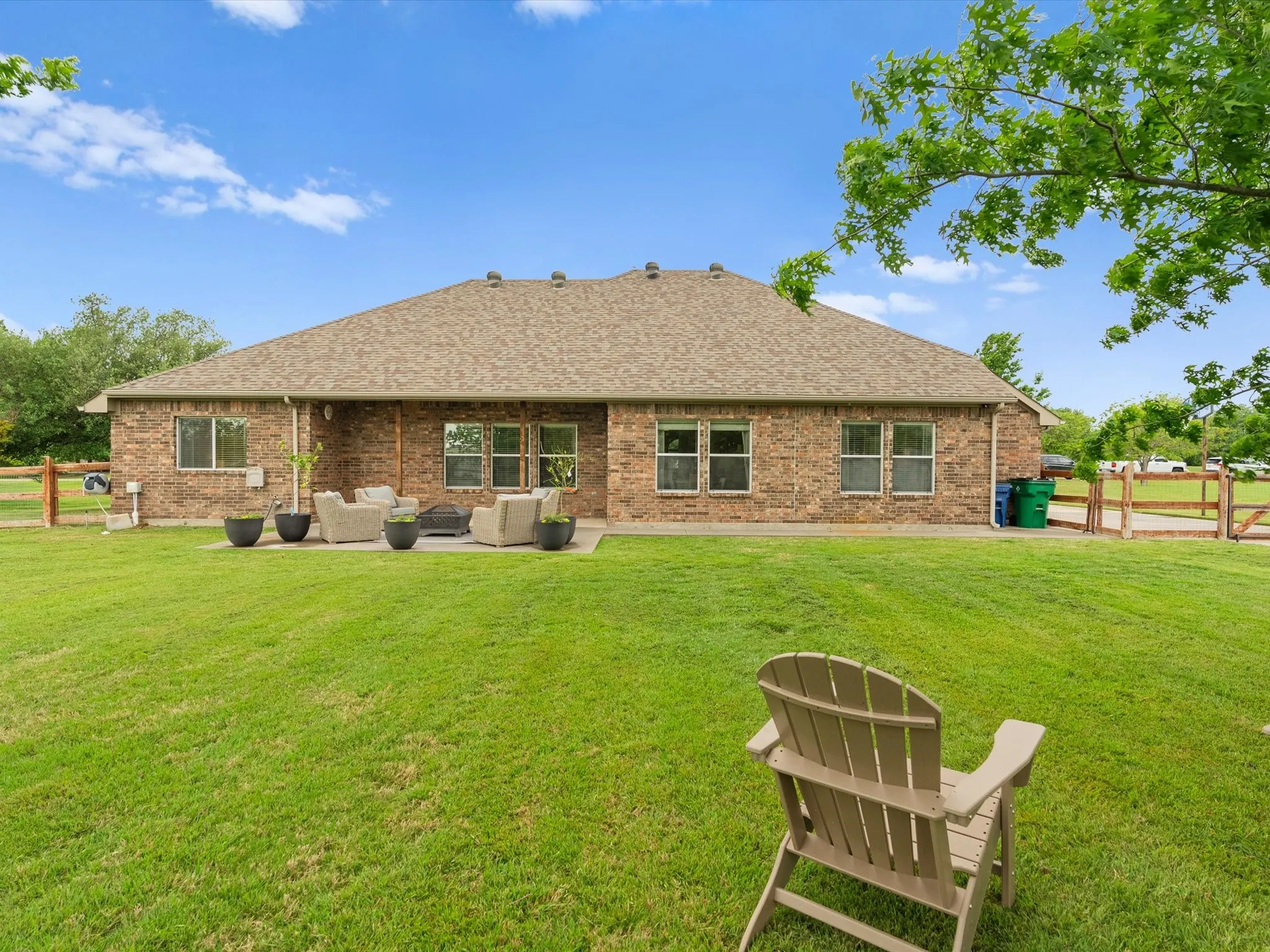 The property features a brick exterior, a patio area with seating, and an expansive lawn
