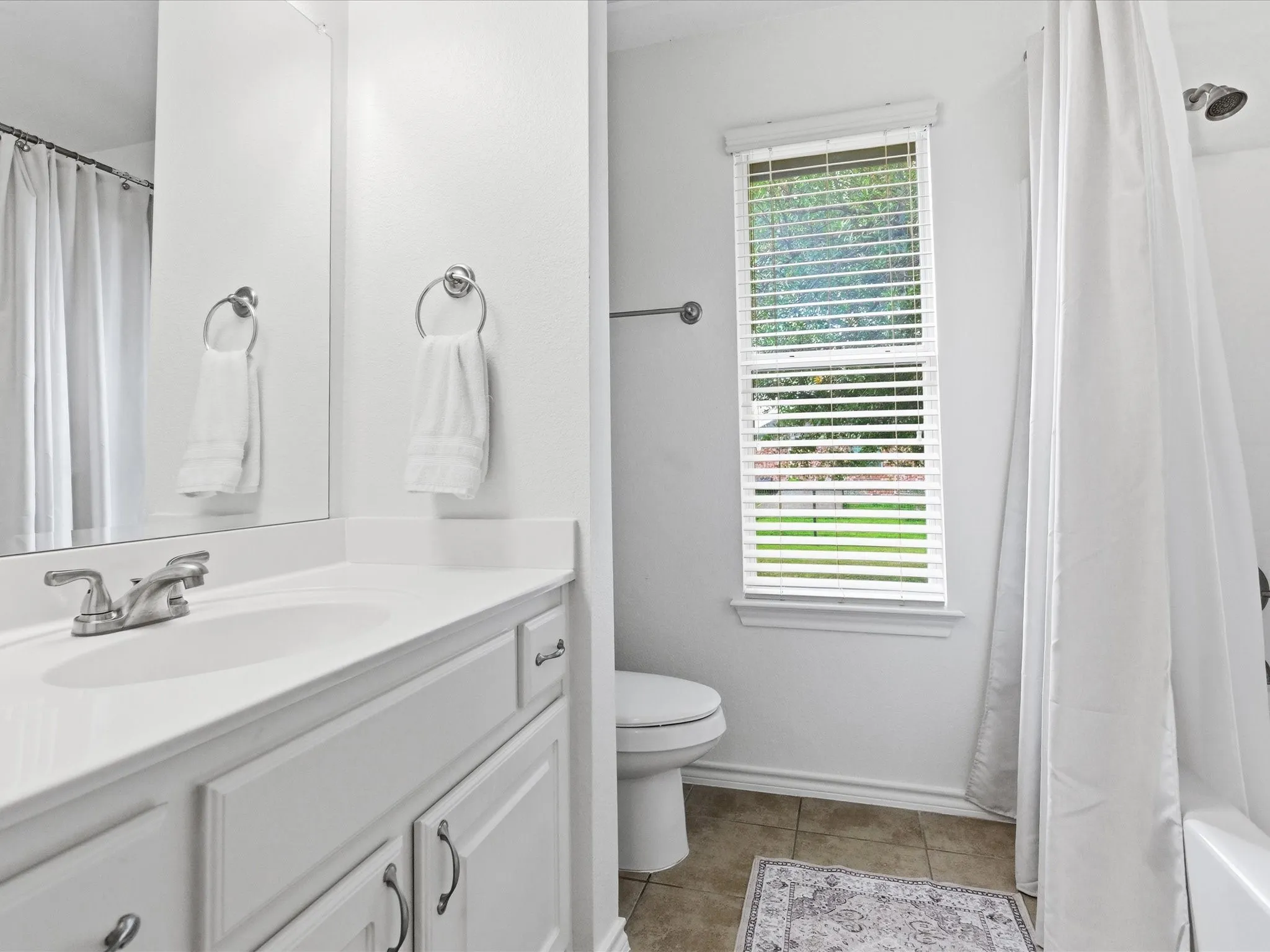 A well-appointed bathroom featuring a vanity with a white countertop and sink, a toilet, and a shower with a white curtain