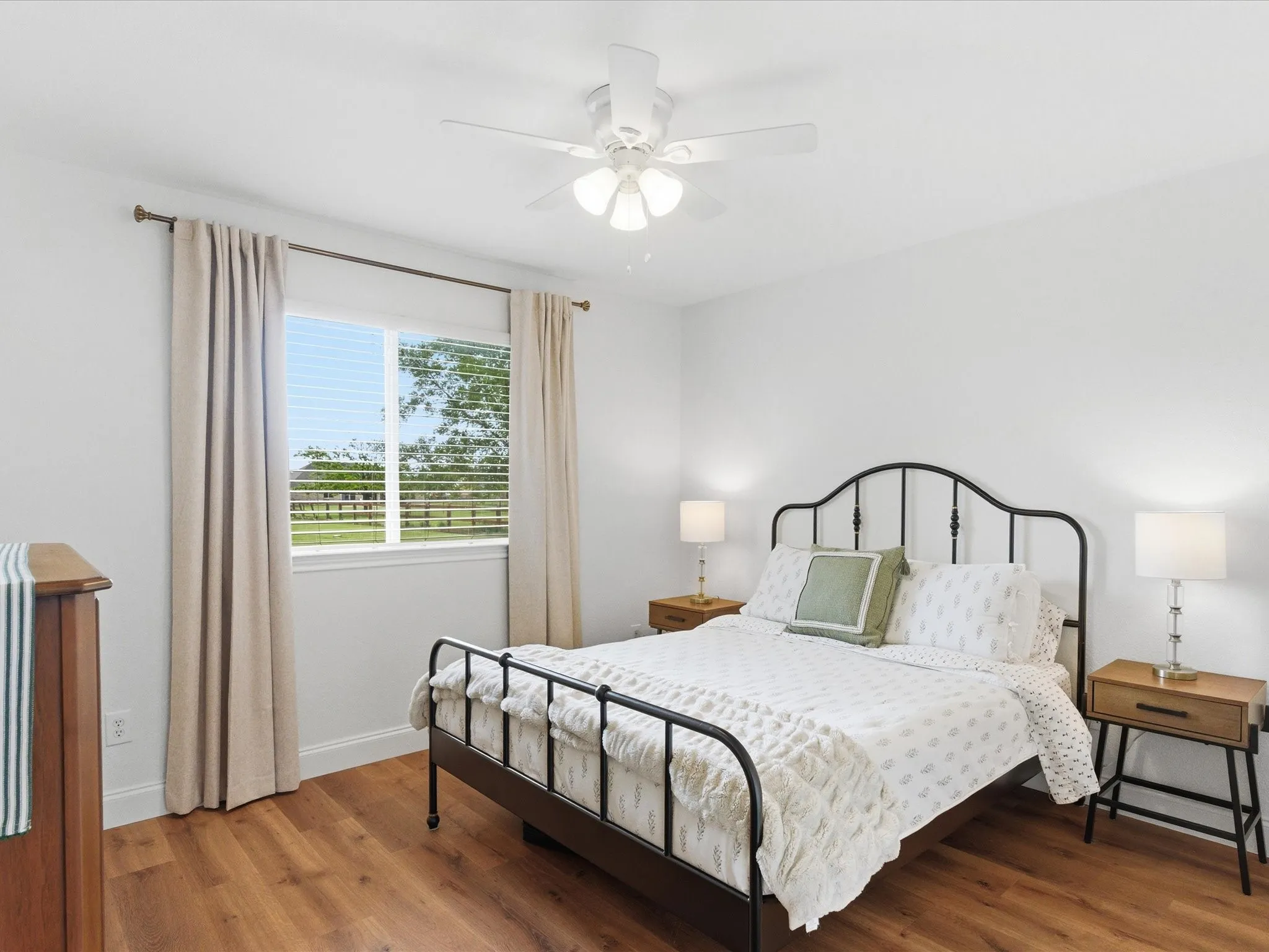 This room features hardwood flooring, a window with blinds and curtains, and a ceiling fan with integrated lighting