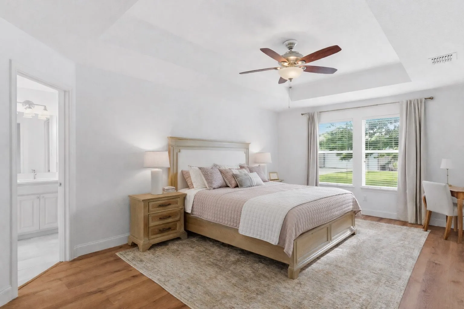 This spacious bedroom features light wood flooring, a tray ceiling, and a ceiling fan