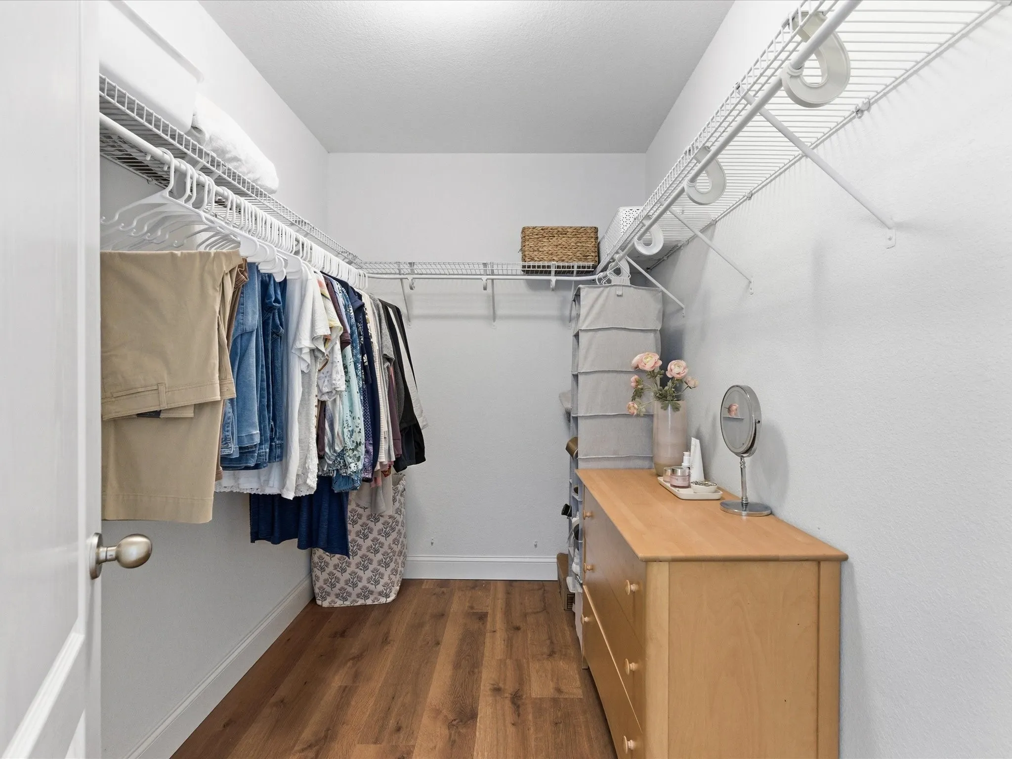 This walk-in closet features hardwood style flooring, white walls, and extensive wire shelving with hanging rods
