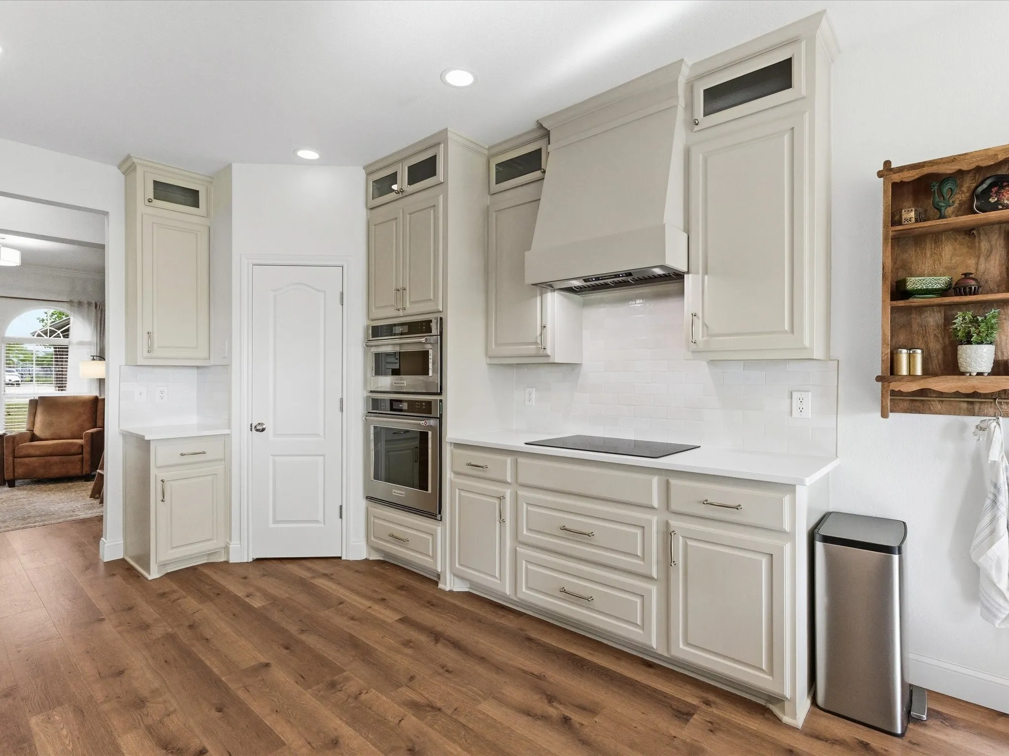 The kitchen features light-colored cabinetry, stainless steel appliances, a built-in oven, a cooktop, and a matching range hood