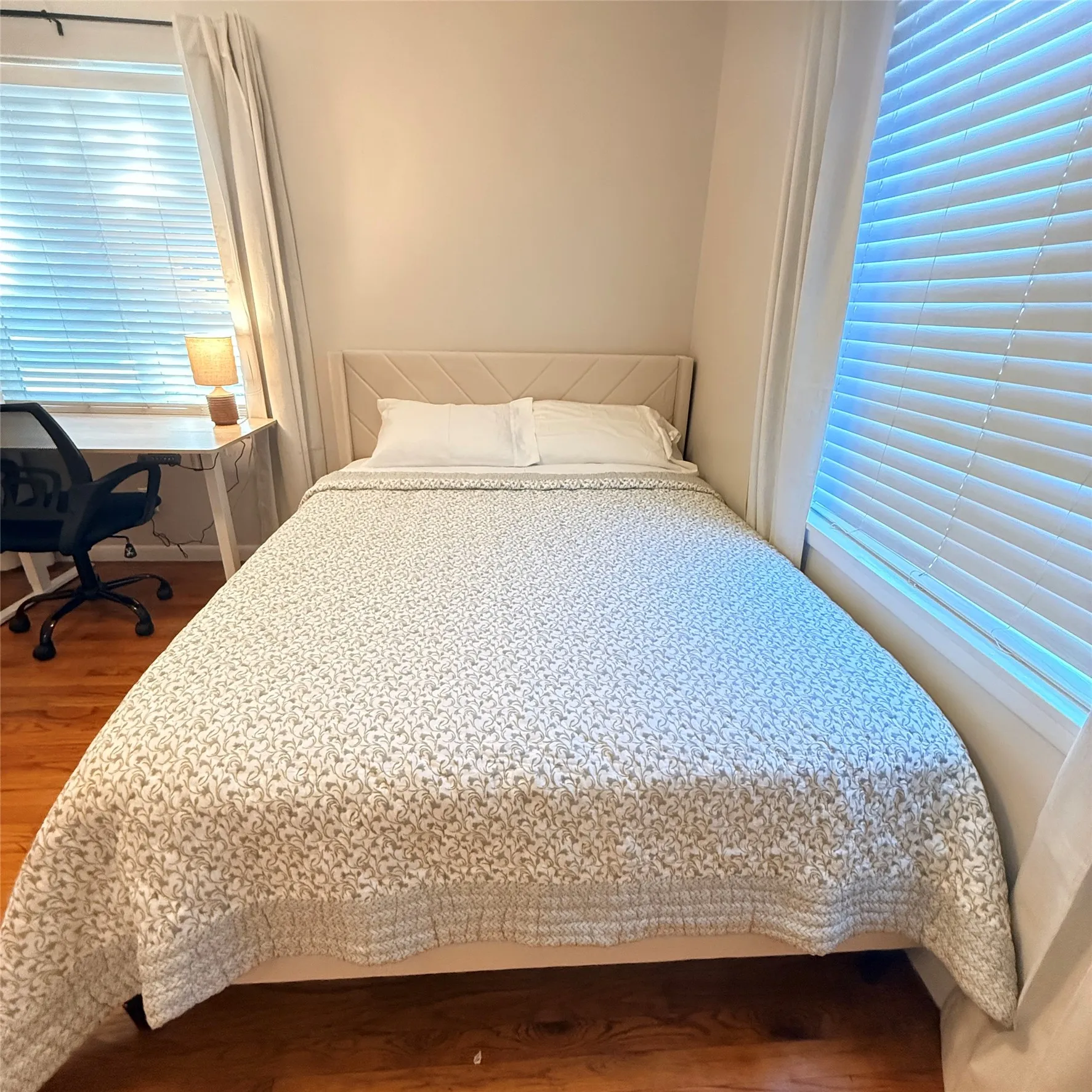 This room features hardwood floors, light-colored walls, and a bed with a neutral-toned upholstered headboard