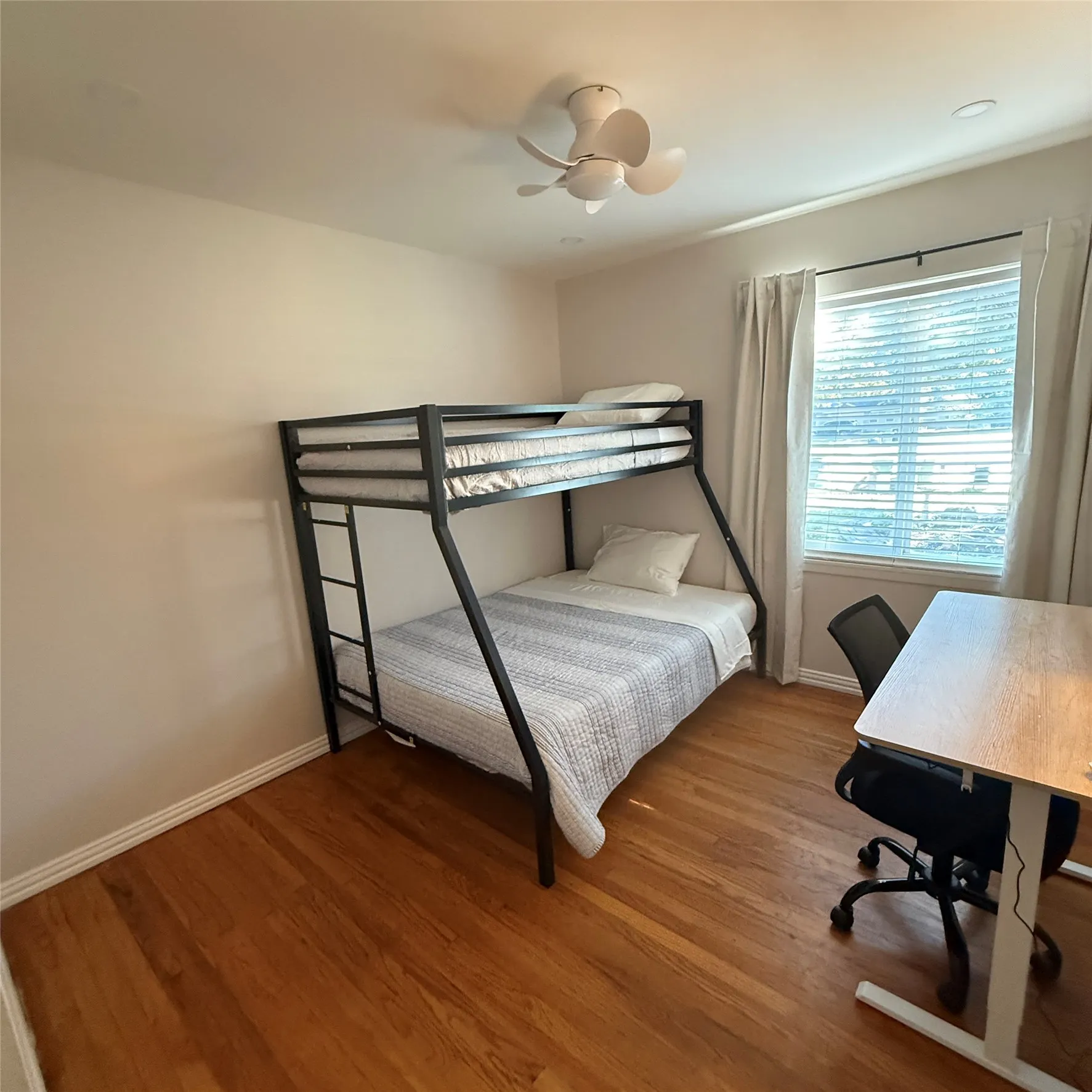 This room features hardwood floors, a white ceiling fan, and a window with blinds and drapes