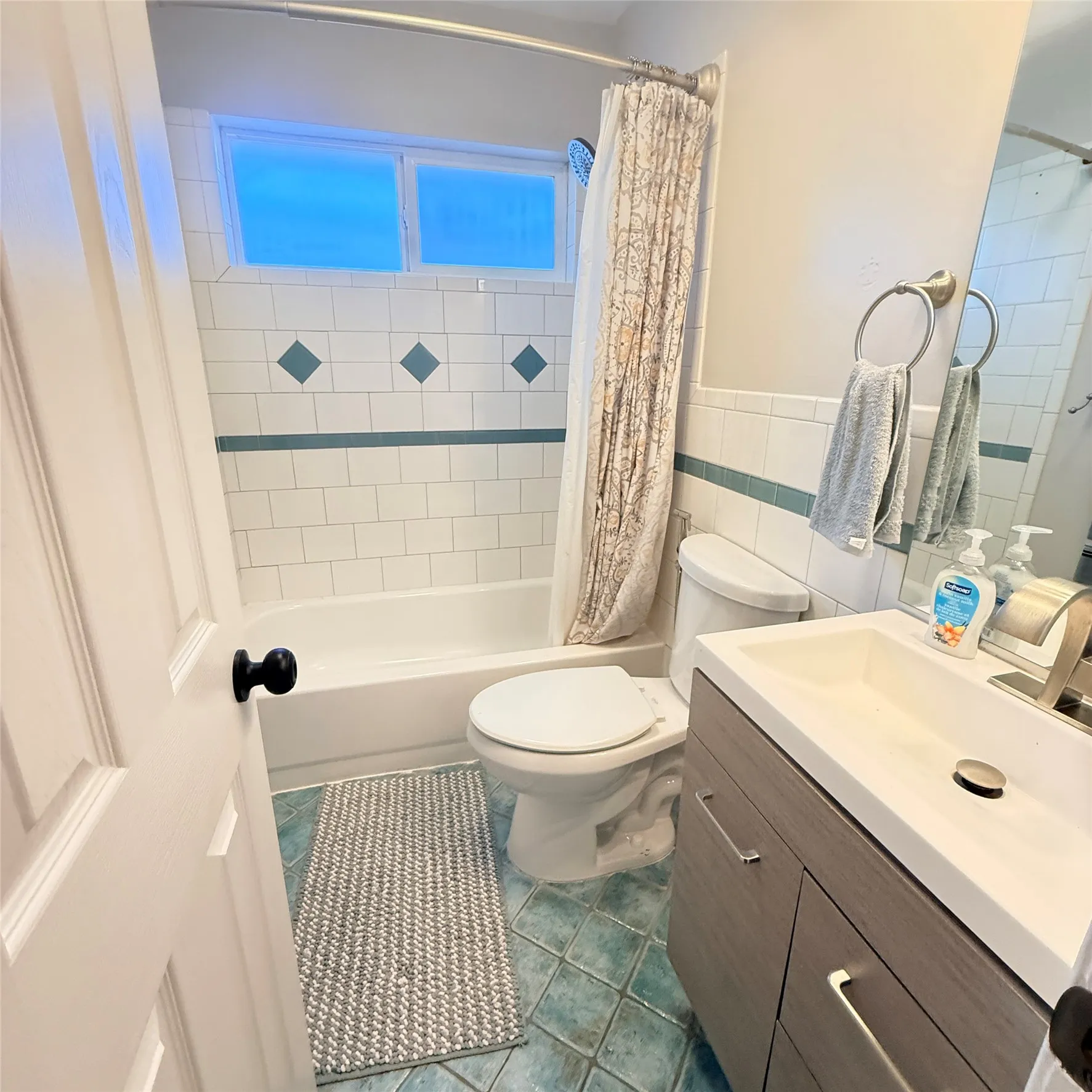 Bathroom featuring a white bathtub and toilet, a light-colored vanity with a rectangular sink, a large mirror, and tiled walls with decorative accents