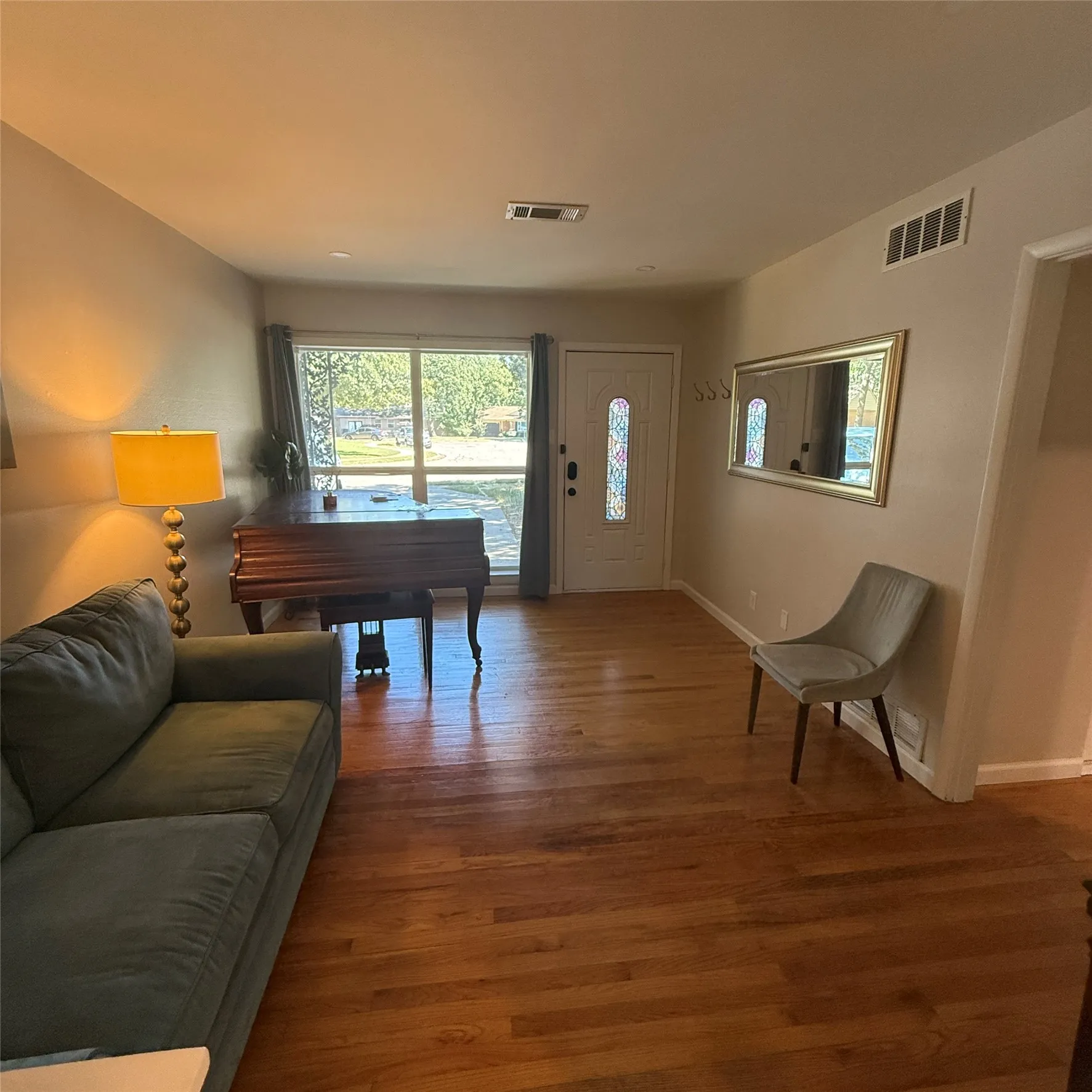 Living area featuring hardwood flooring, a large window, and a white front door with a decorative glass insert