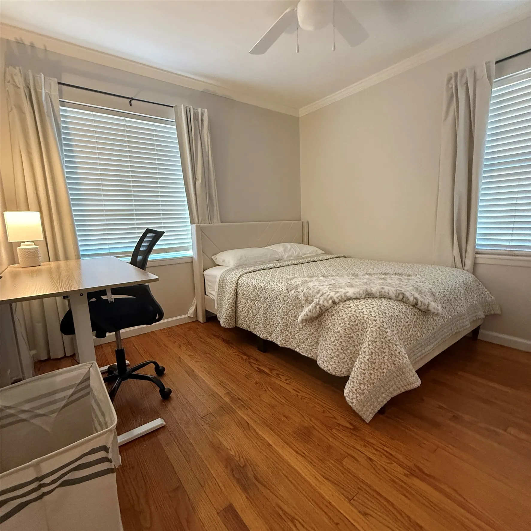 This room features wood flooring, a ceiling fan, and two windows with blinds and curtains