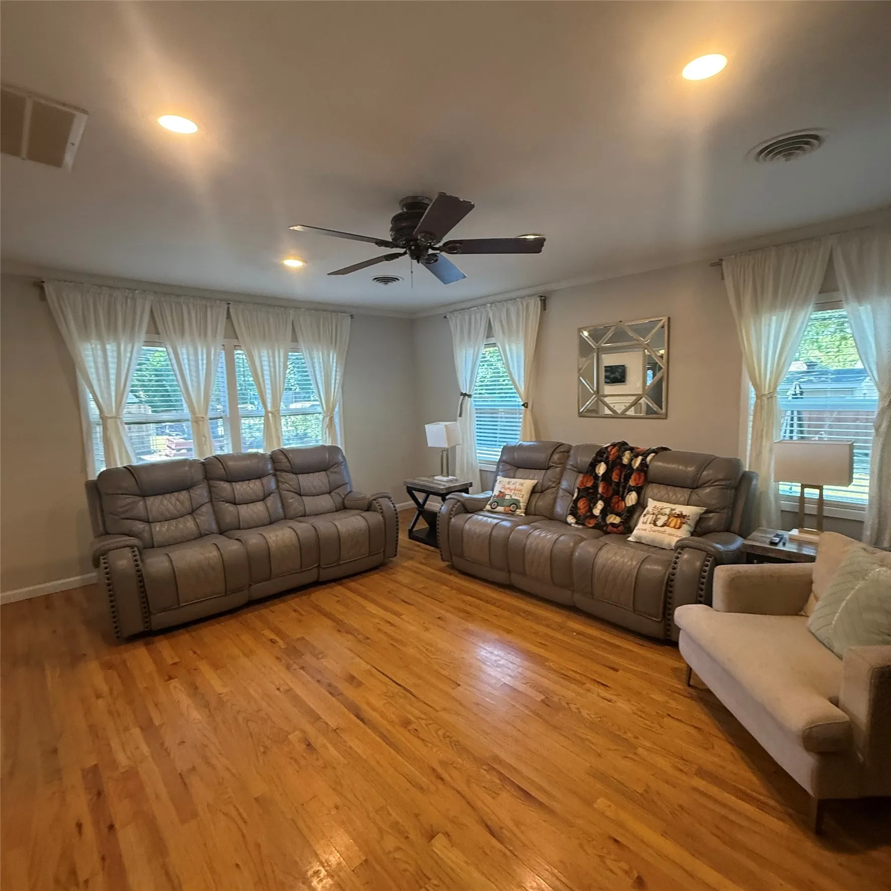 Living area featuring hardwood floors, recessed lighting, a ceiling fan, and multiple windows with blinds and sheer curtains