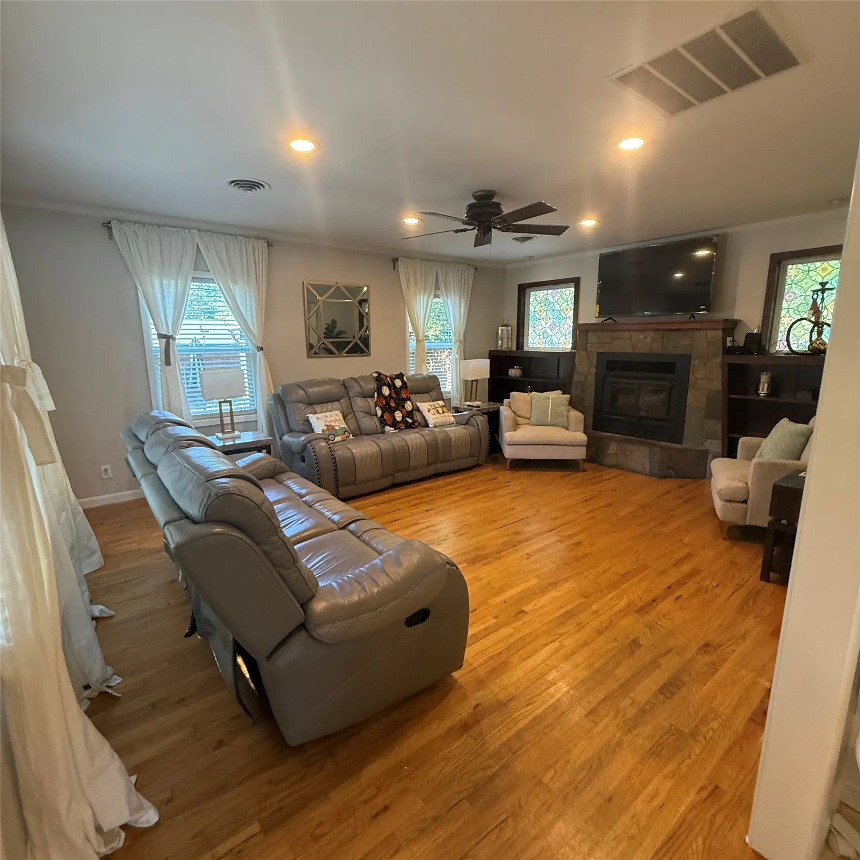Living room featuring hardwood floors, a stone-faced fireplace, and recessed lighting