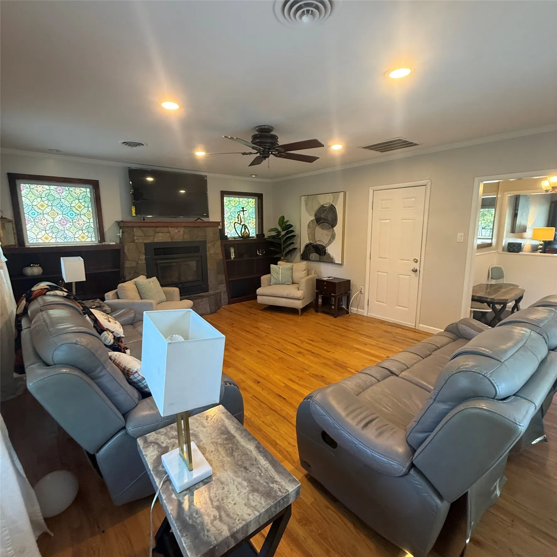 This living space features hardwood floors, a stone-faced fireplace, and recessed lighting