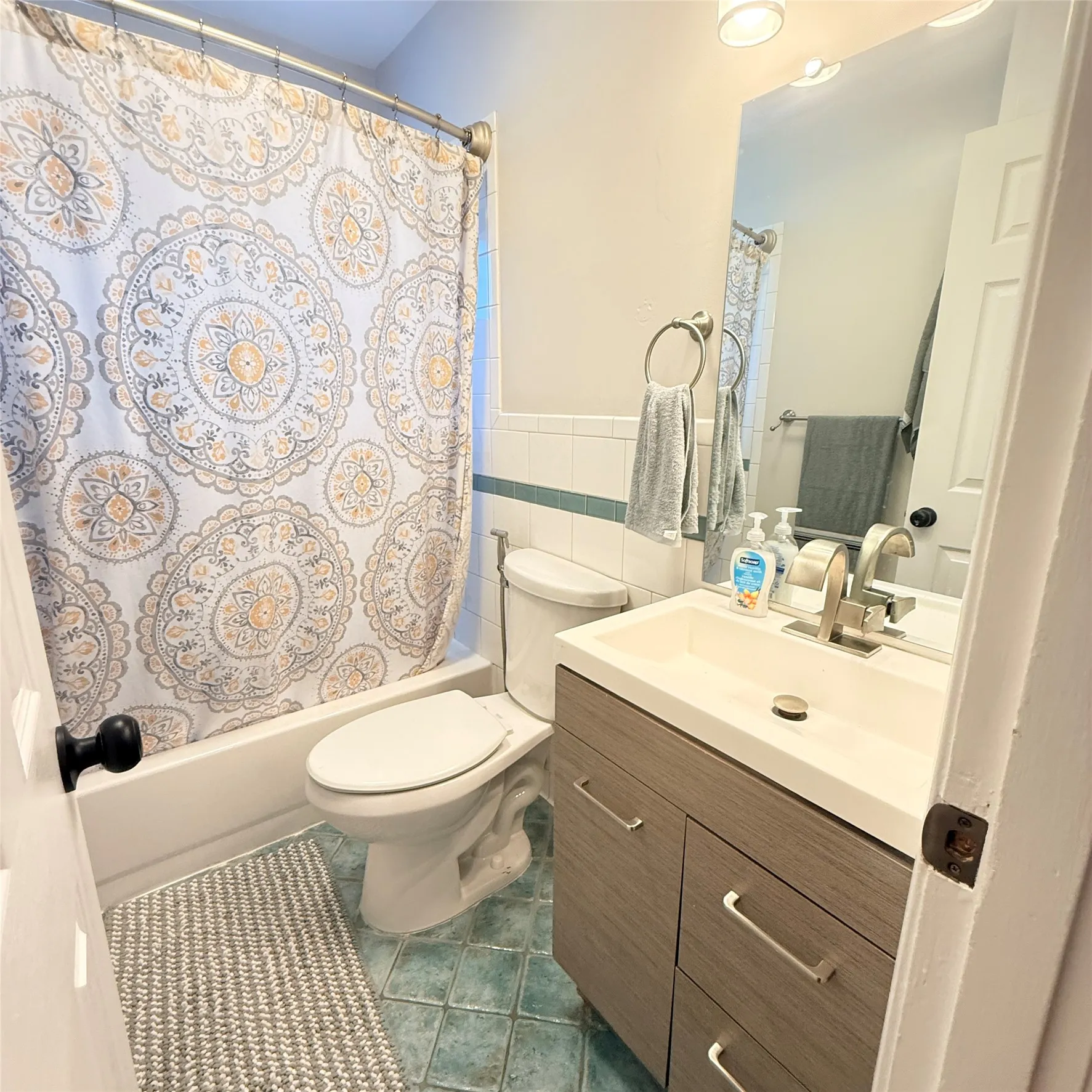 Bathroom featuring a vanity with a white countertop sink and a modern faucet, a toilet, a bathtub with a shower, and tiled flooring