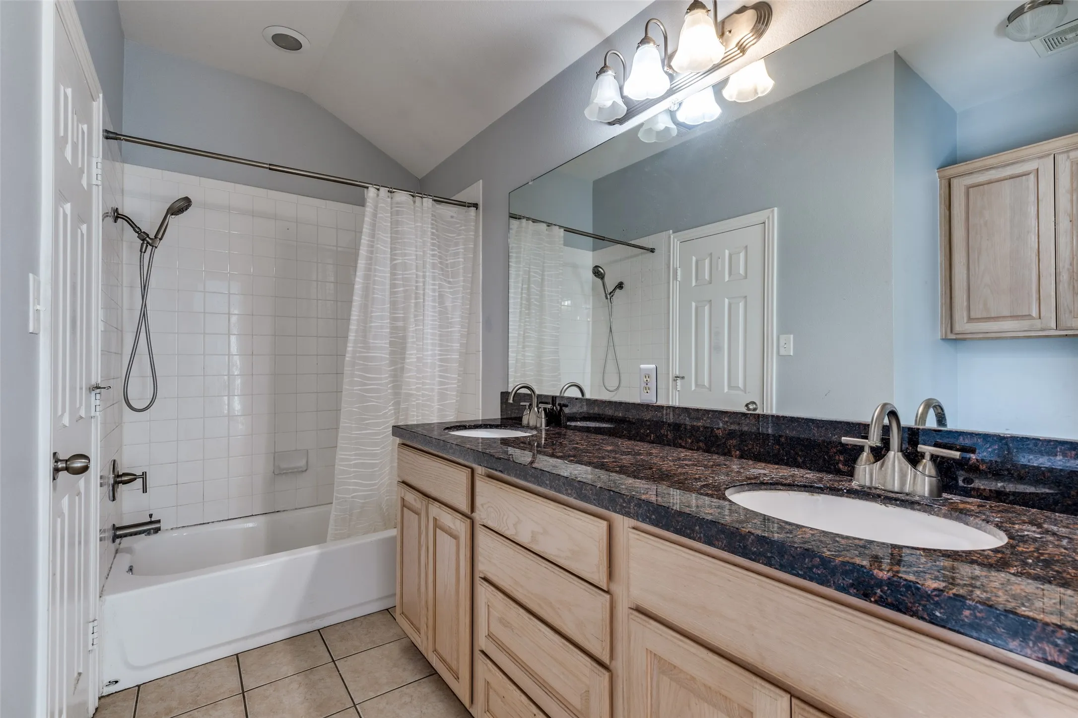 The bathroom features a double vanity with a dark granite countertop, a bathtub with white subway tile surround, and light wood cabinetry