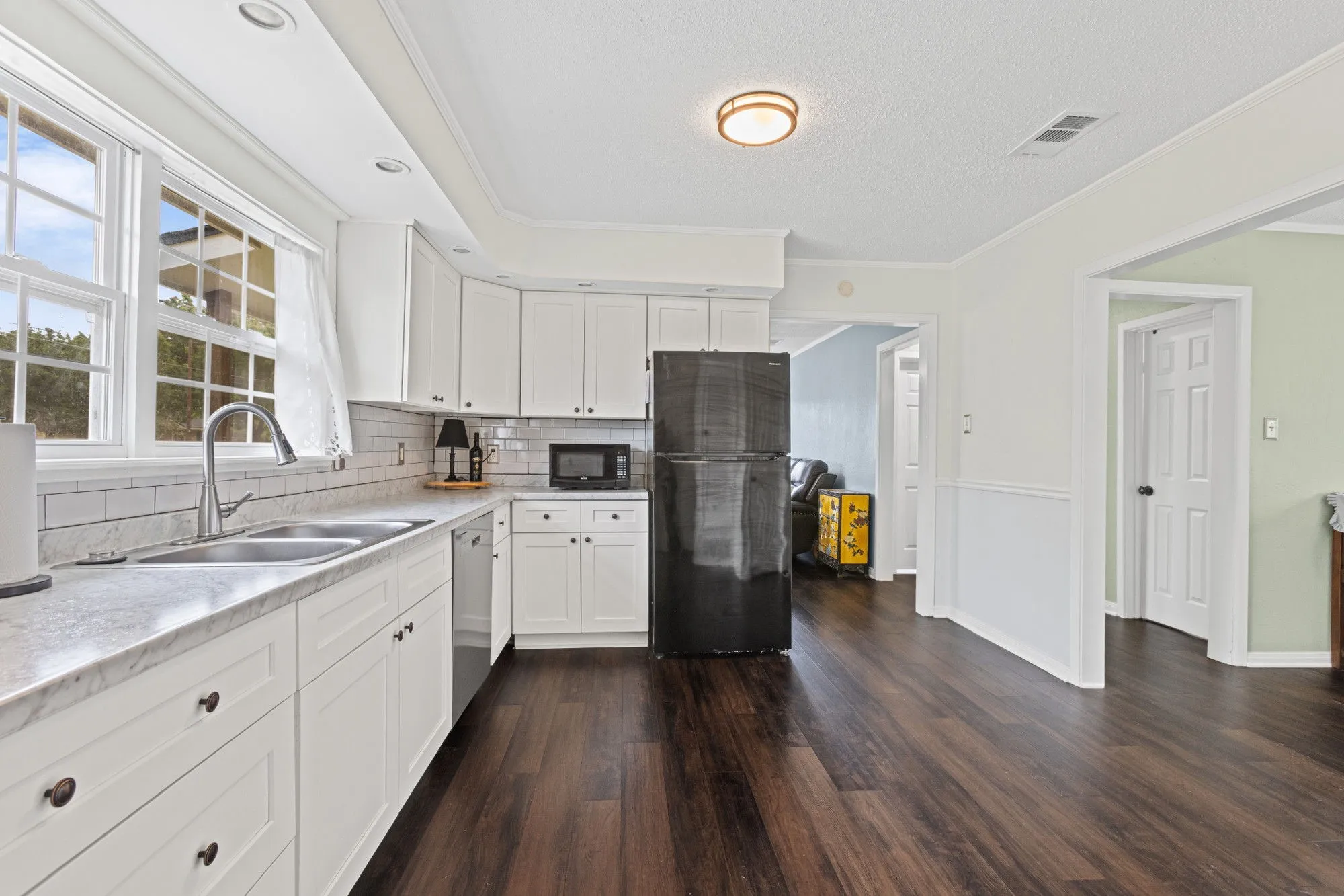Kitchen featuring black appliances, white cabinetry, ornamental molding, decorative backsplash, and dark wood-style flooring