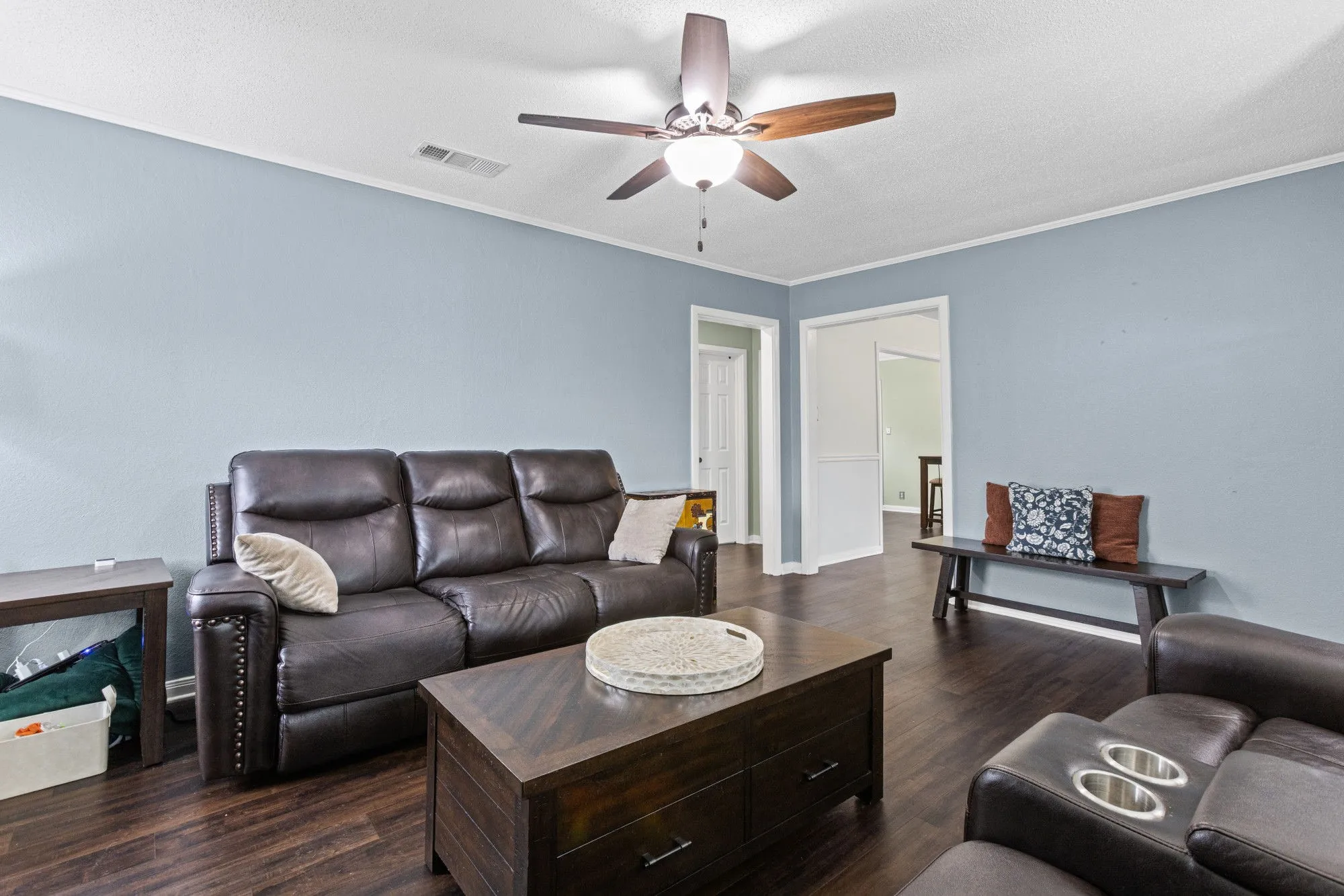 Living room featuring dark wood-style floors, ornamental molding, ceiling fan, and a textured ceiling