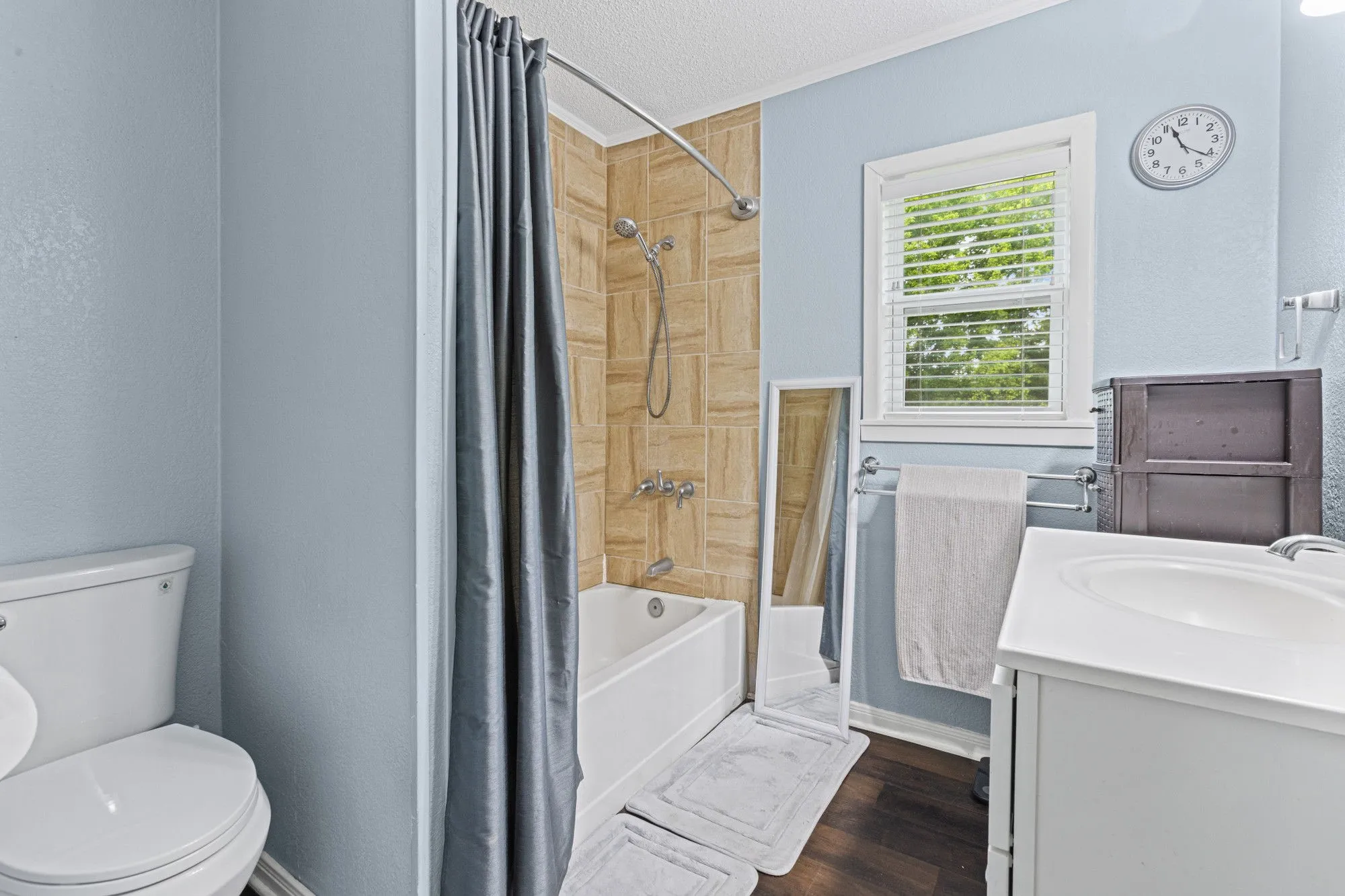 Full bathroom with vanity, a textured ceiling, shower / bathtub combination with curtain, and dark wood-type flooring