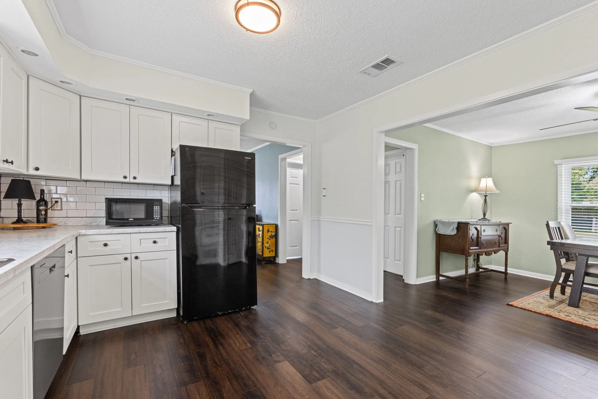 Kitchen with black appliances, crown molding, a textured ceiling, white cabinets, and dark wood finished floors