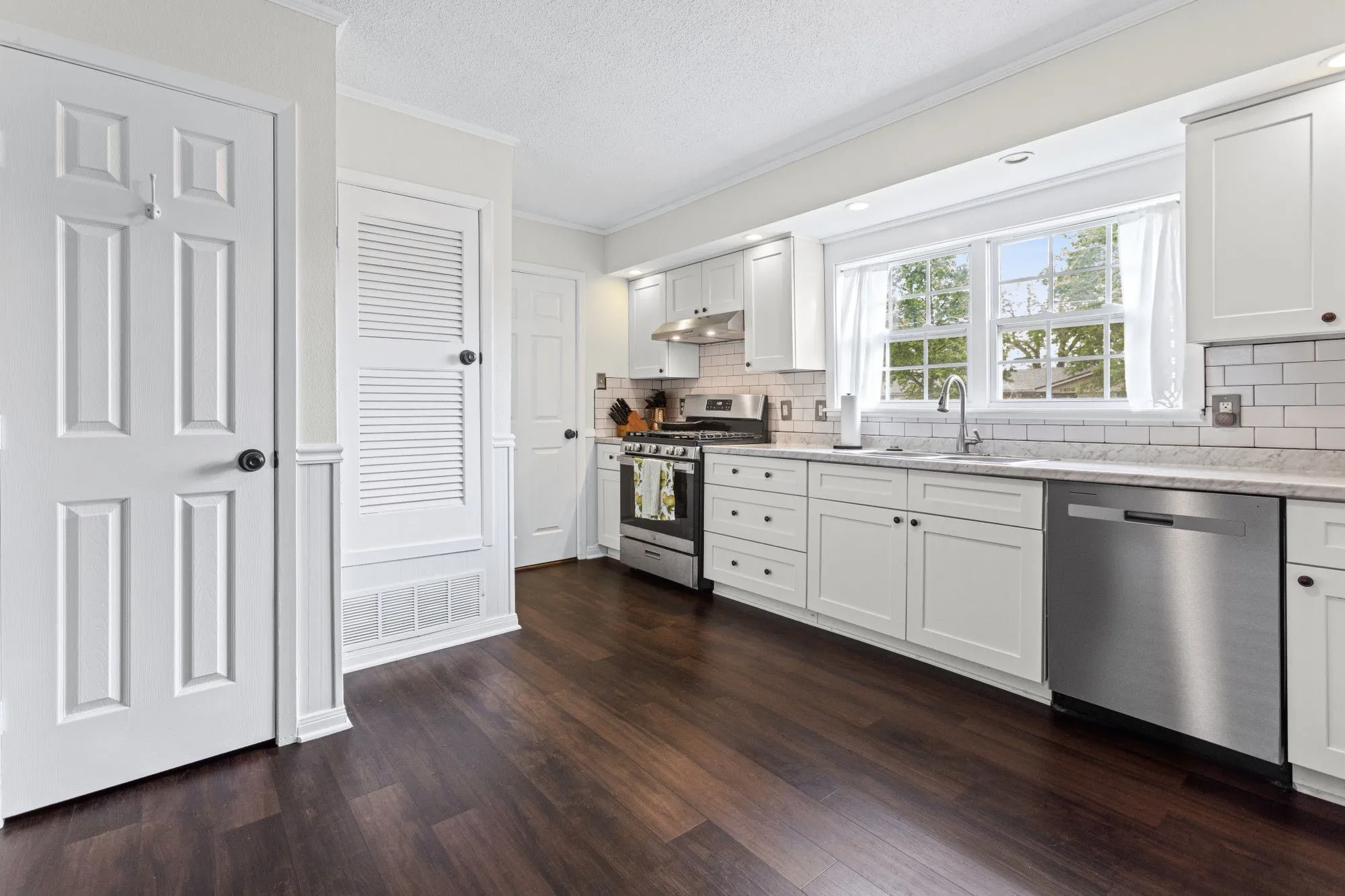 Kitchen with ornamental molding, stainless steel appliances, white cabinets, light stone countertops, and dark wood-style floors