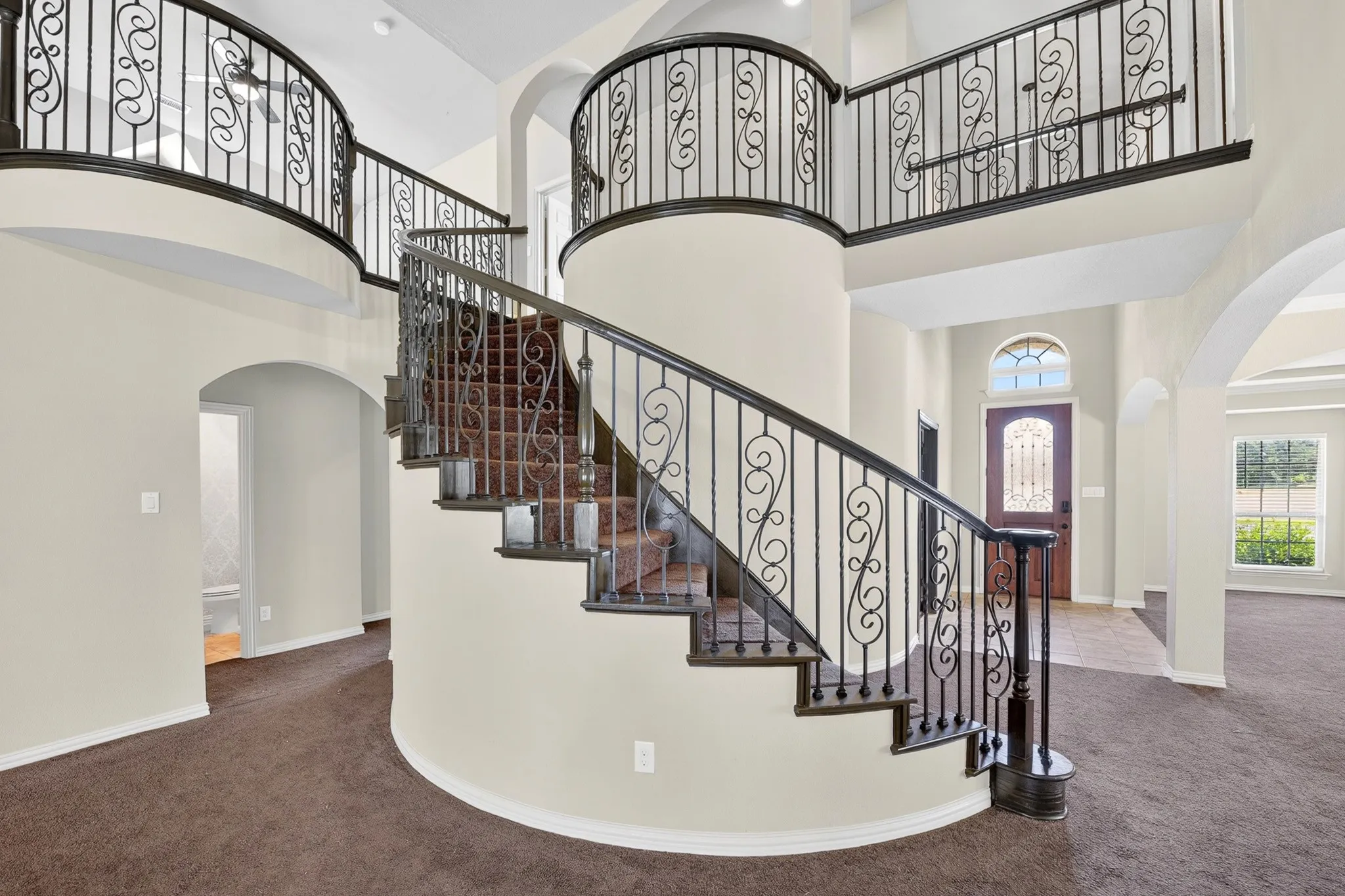 Grand foyer featuring a curved staircase with wrought iron railings and a balcony overlooking the space