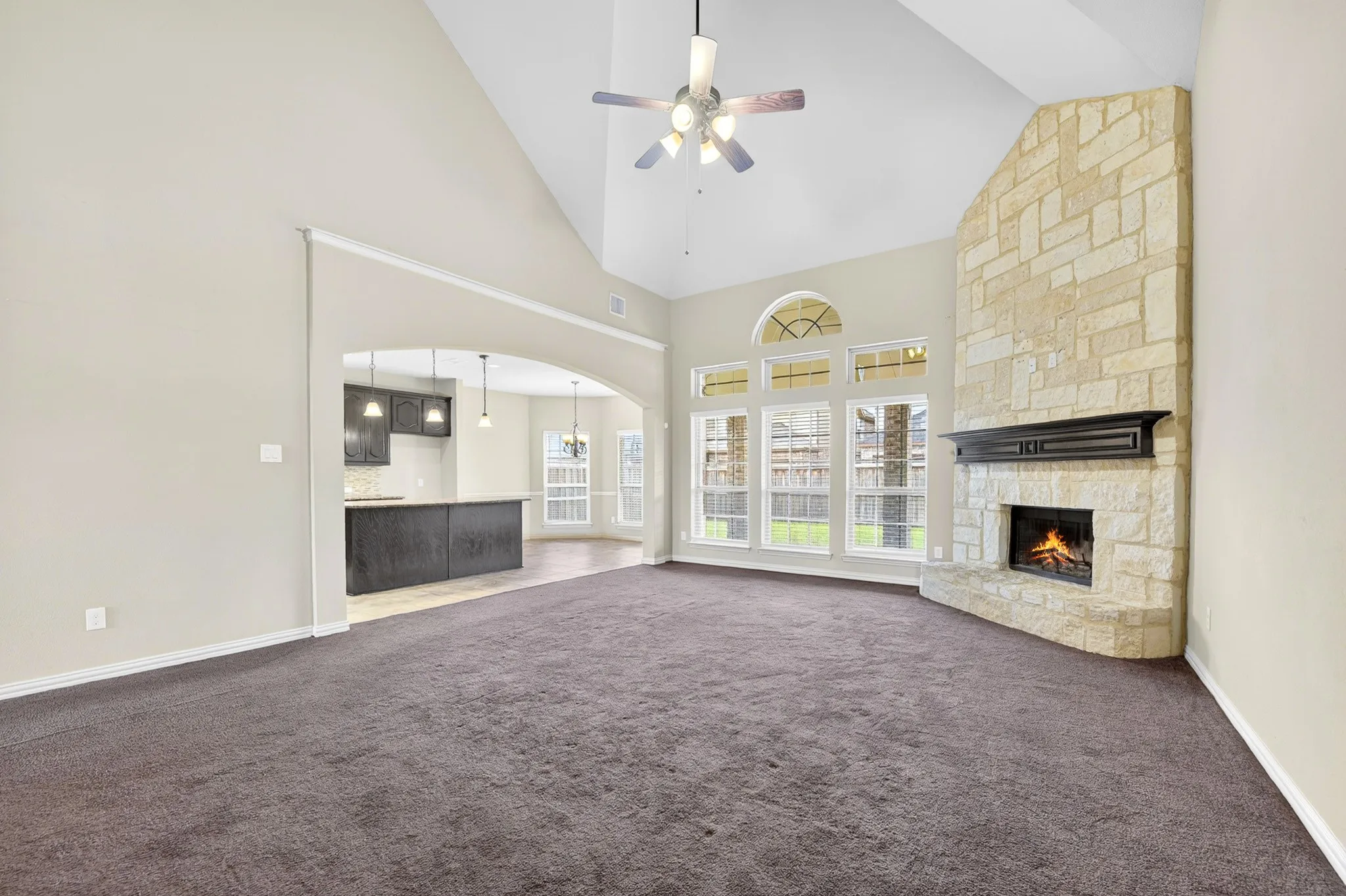 Living area featuring vaulted ceilings, a ceiling fan, and a floor-to-ceiling stone fireplace with a mantle