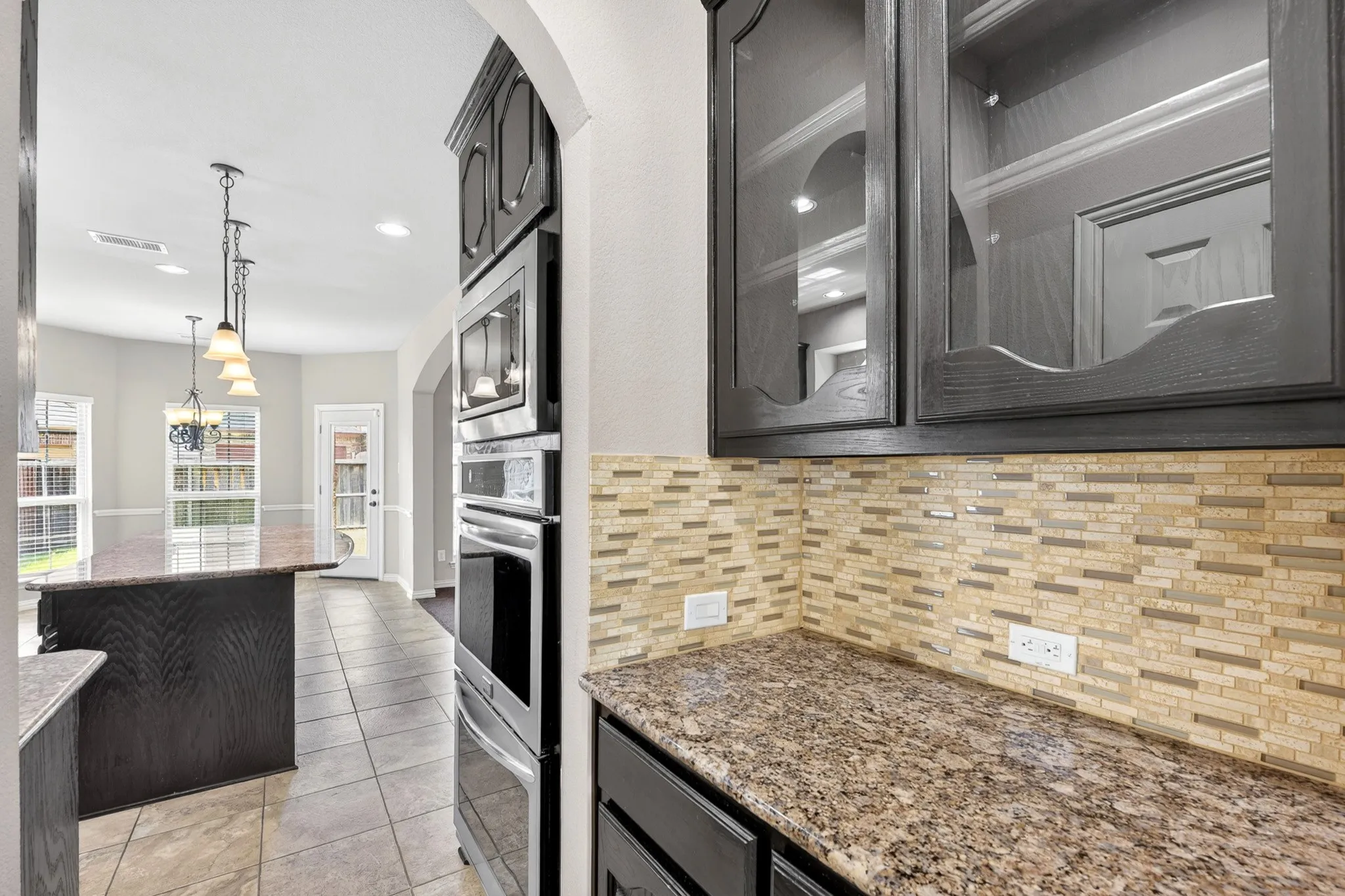 Kitchen featuring granite countertops, a tiled backsplash, dark wood cabinetry, and stainless steel built-in appliances