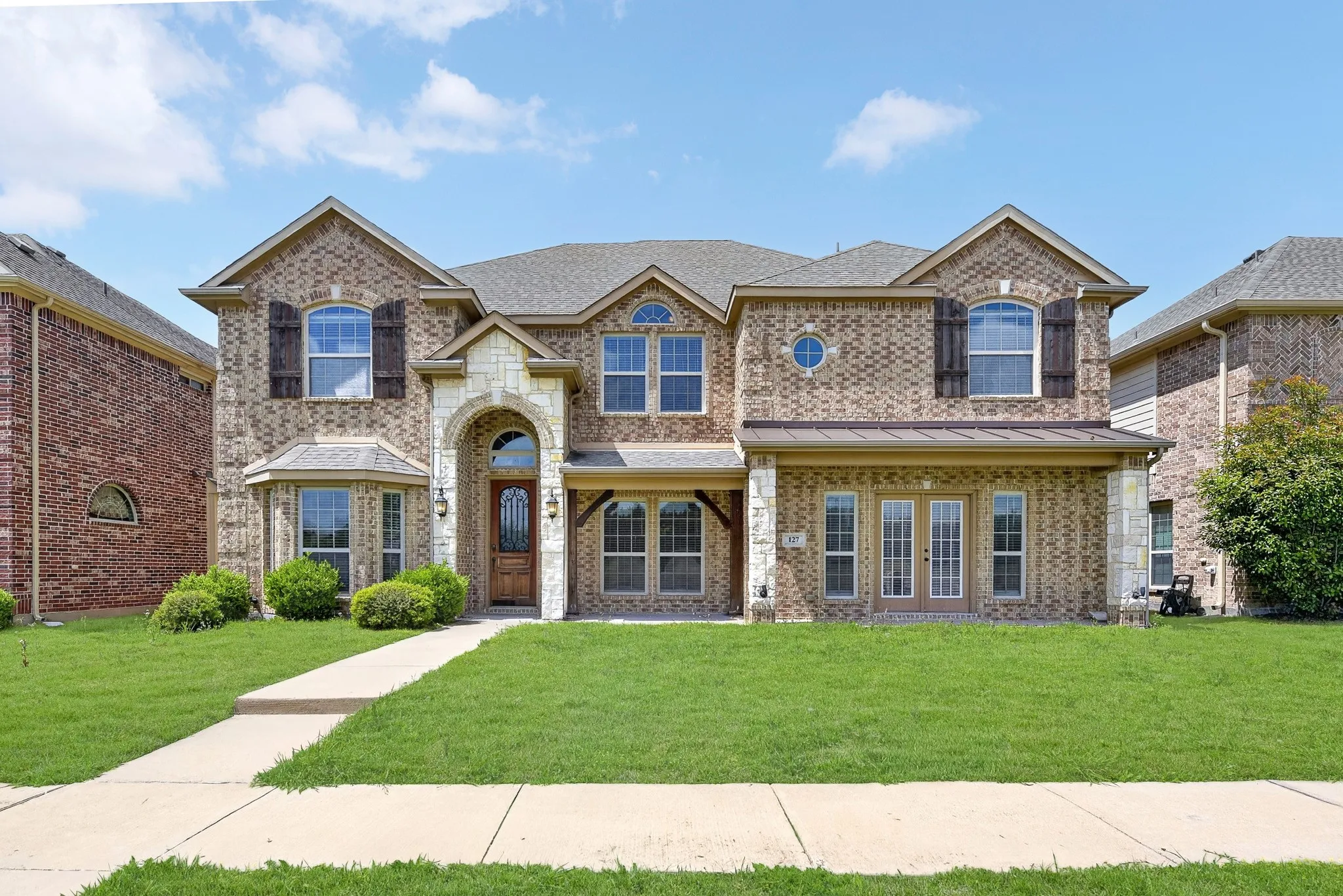 The property features a brick exterior with stone accents, a well-maintained lawn, and a concrete pathway leading to the entrance