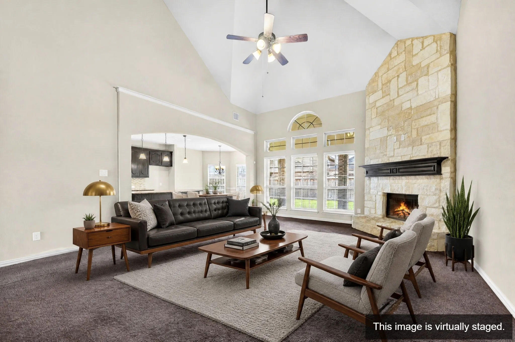 Great room featuring vaulted ceilings, a stone-clad fireplace with a dark wood mantel, and expansive windows