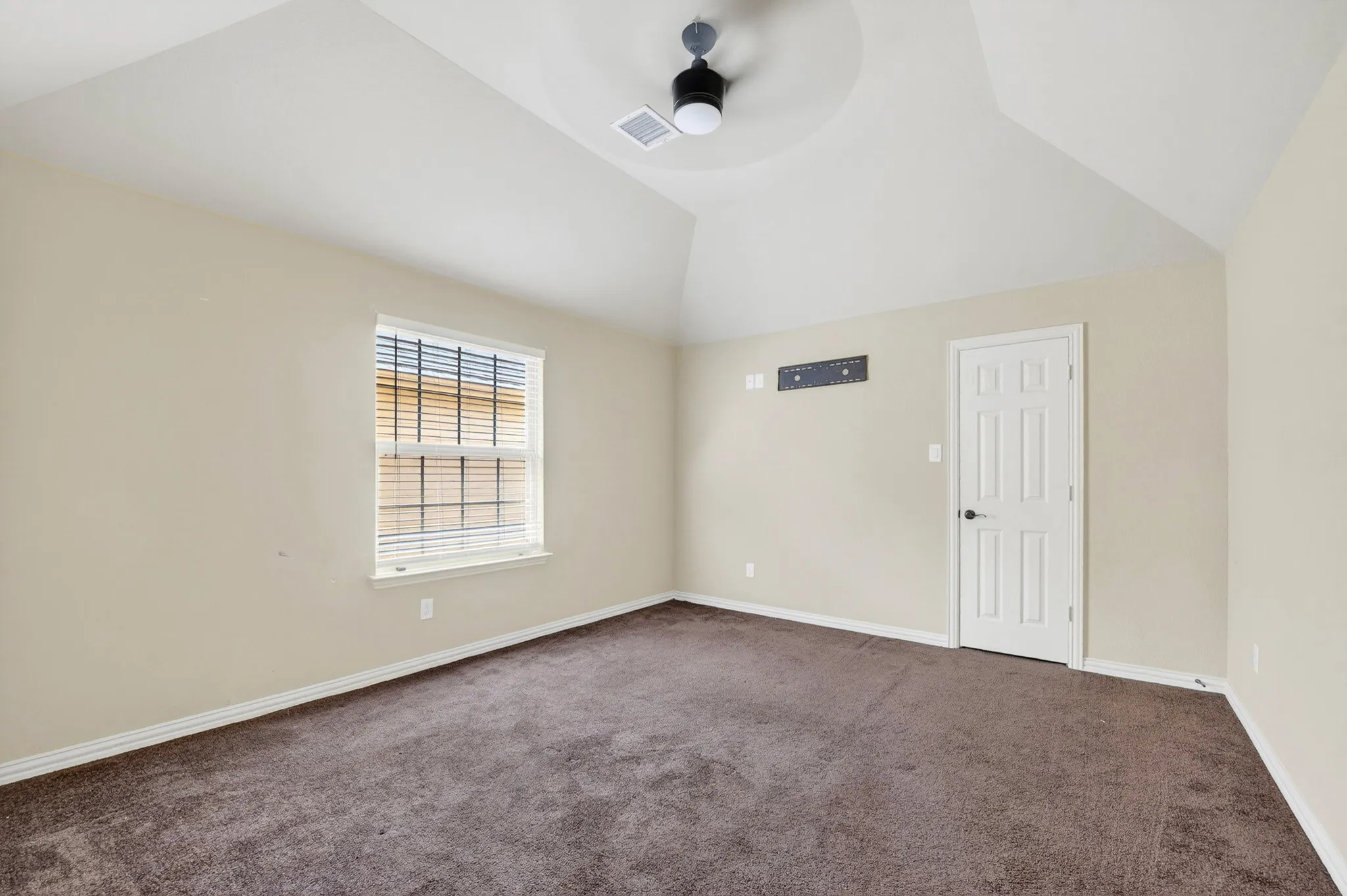 This room features a vaulted ceiling with a ceiling fan, a window with blinds, and carpeted flooring
