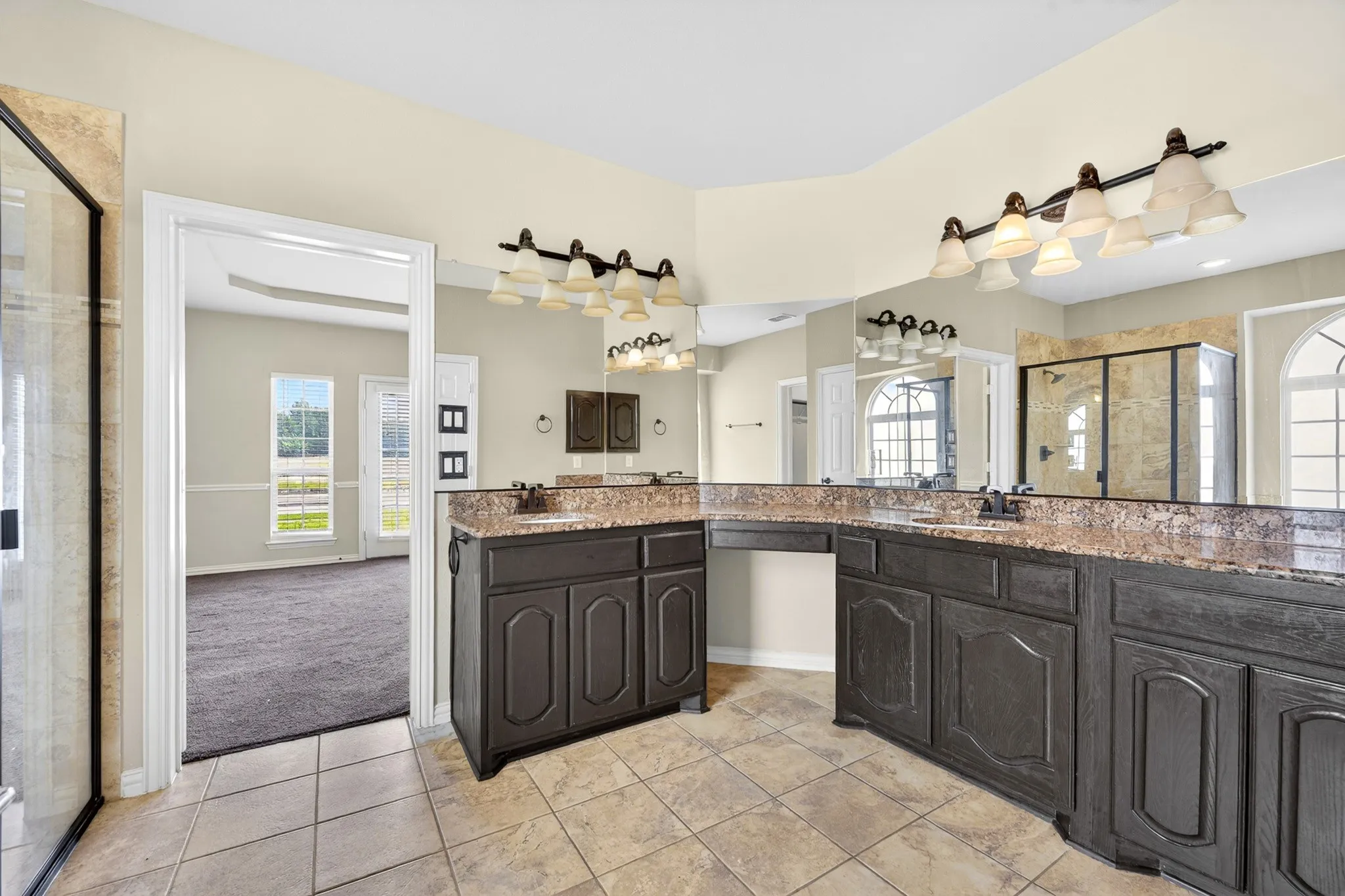 The bathroom features dual vanities with dark cabinetry and granite countertops, complemented by a large mirror and tiled flooring
