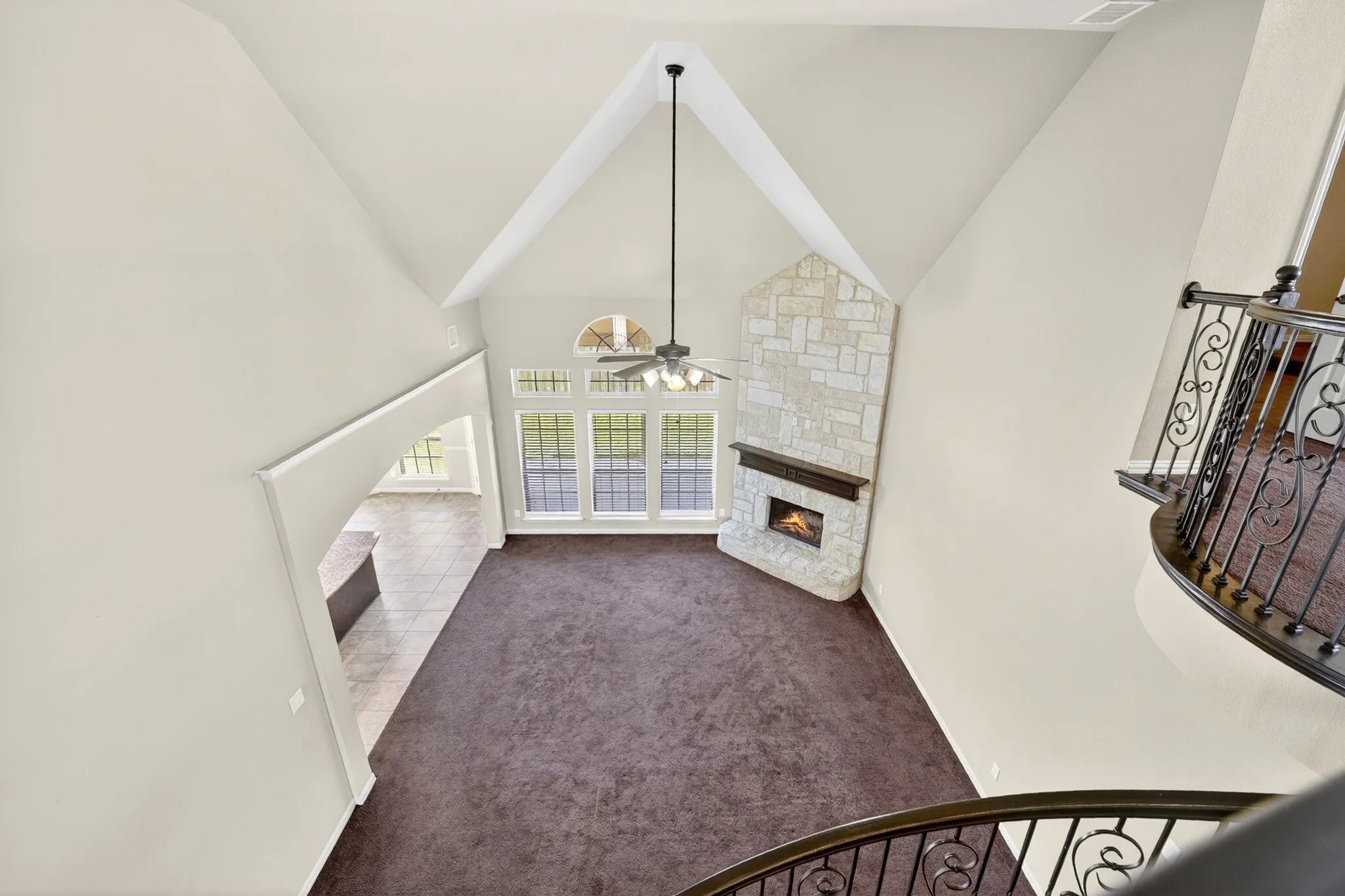 Spacious living area featuring a vaulted ceiling, a stone fireplace, large windows, and a ceiling fan