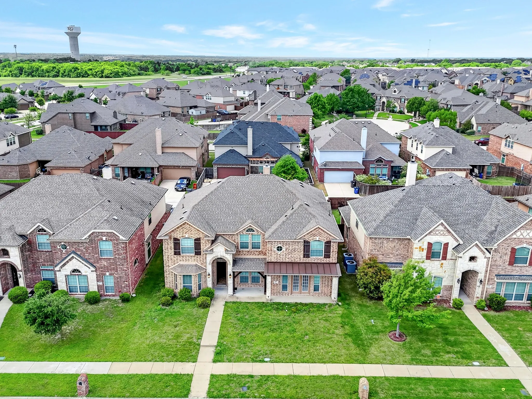 Aerial view showcasing a residential neighborhood with numerous properties featuring brick and stone exteriors, shingled roofs, and well-maintained lawns