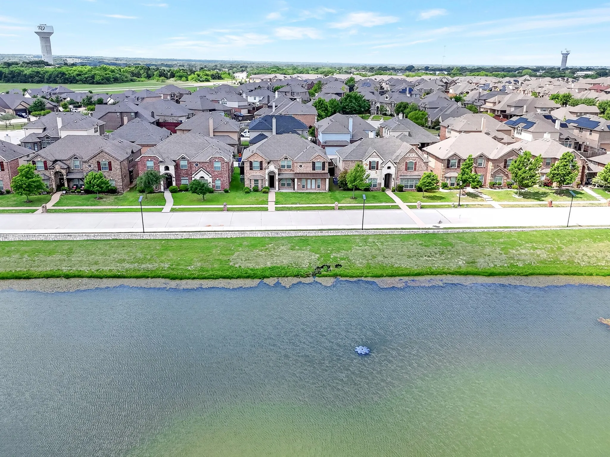The property is part of a neighborhood featuring residential homes with brick facades and well-maintained lawns, situated across from a body of water with a fountain