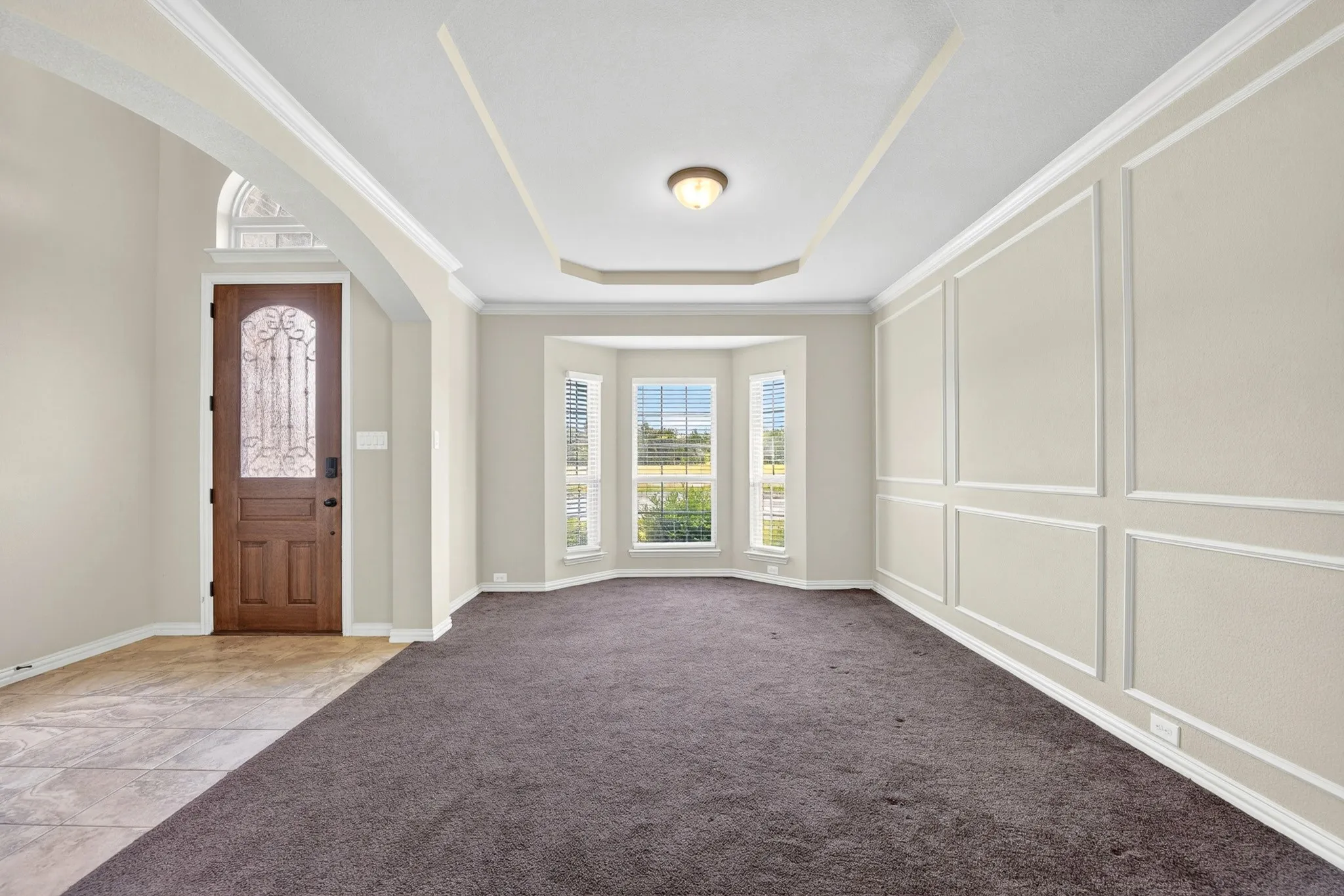 This inviting room features a decorative wood front door with an arched transom, a tray ceiling, and a bay window providing natural light