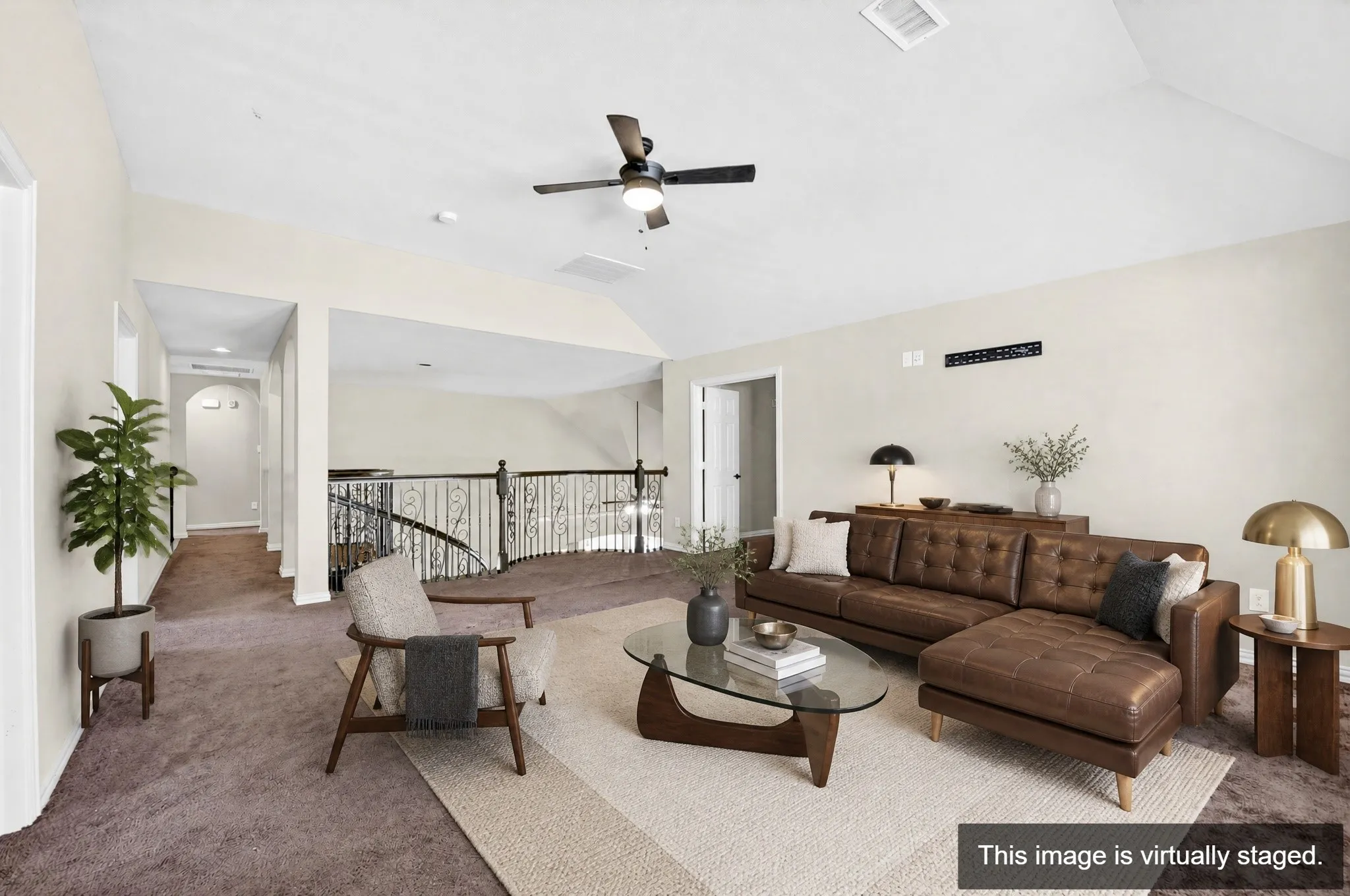 Spacious loft area featuring vaulted ceilings, carpet flooring, decorative railing, and a ceiling fan