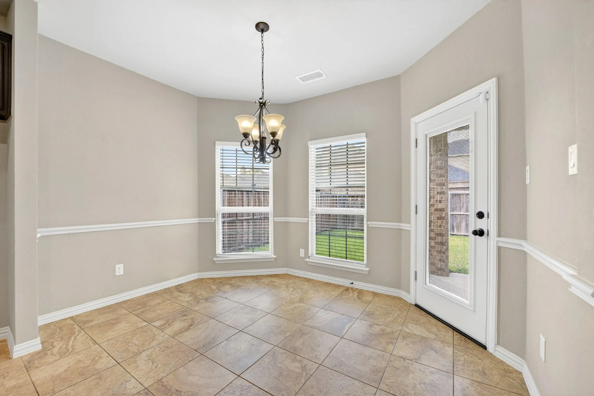 This space features tile flooring, two windows with blinds, a glass-paned door, and a chandelier