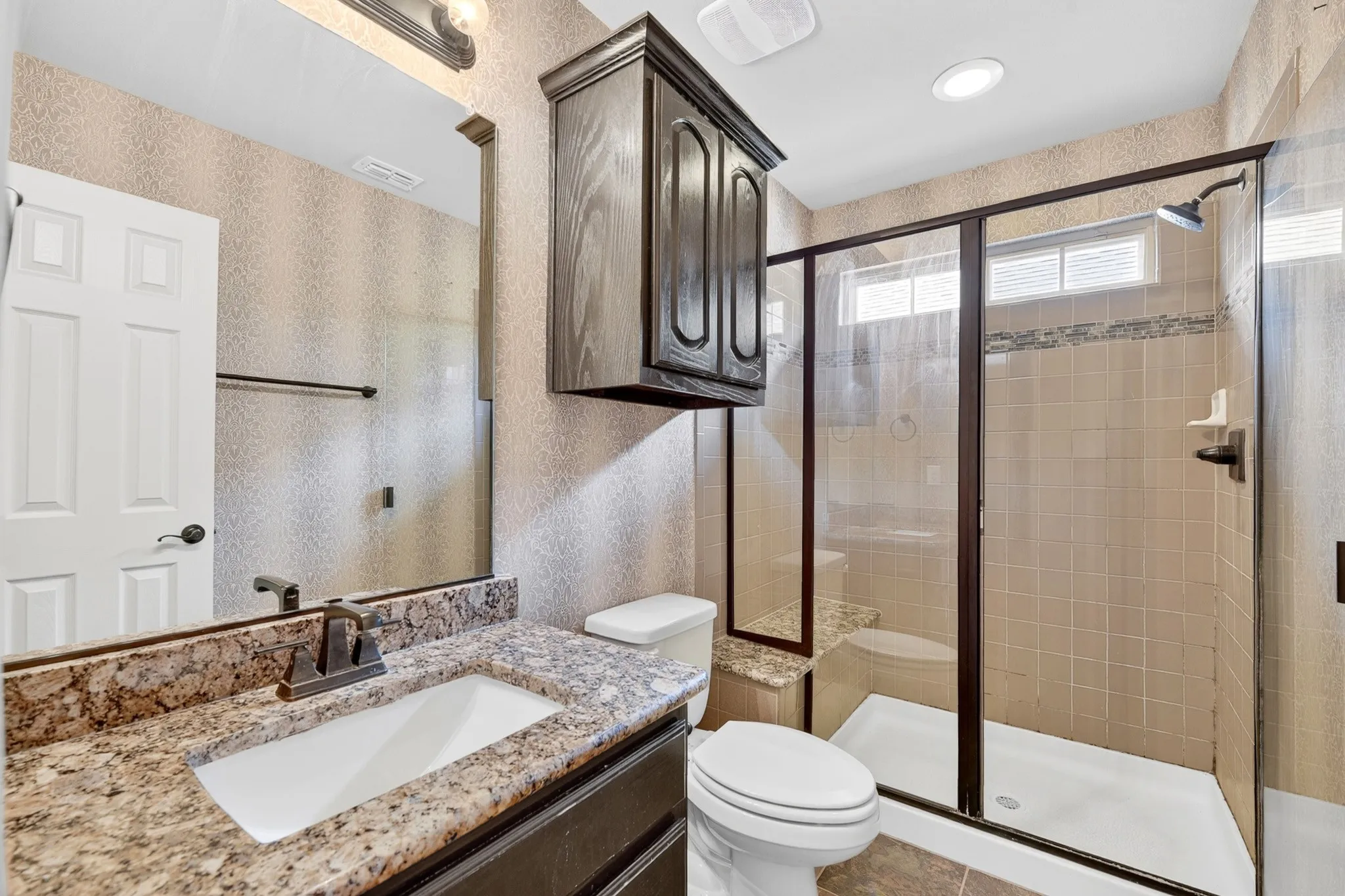 The bathroom features a vanity with a granite countertop and an integrated sink, a glass-enclosed shower with tiled walls, and a window providing natural light