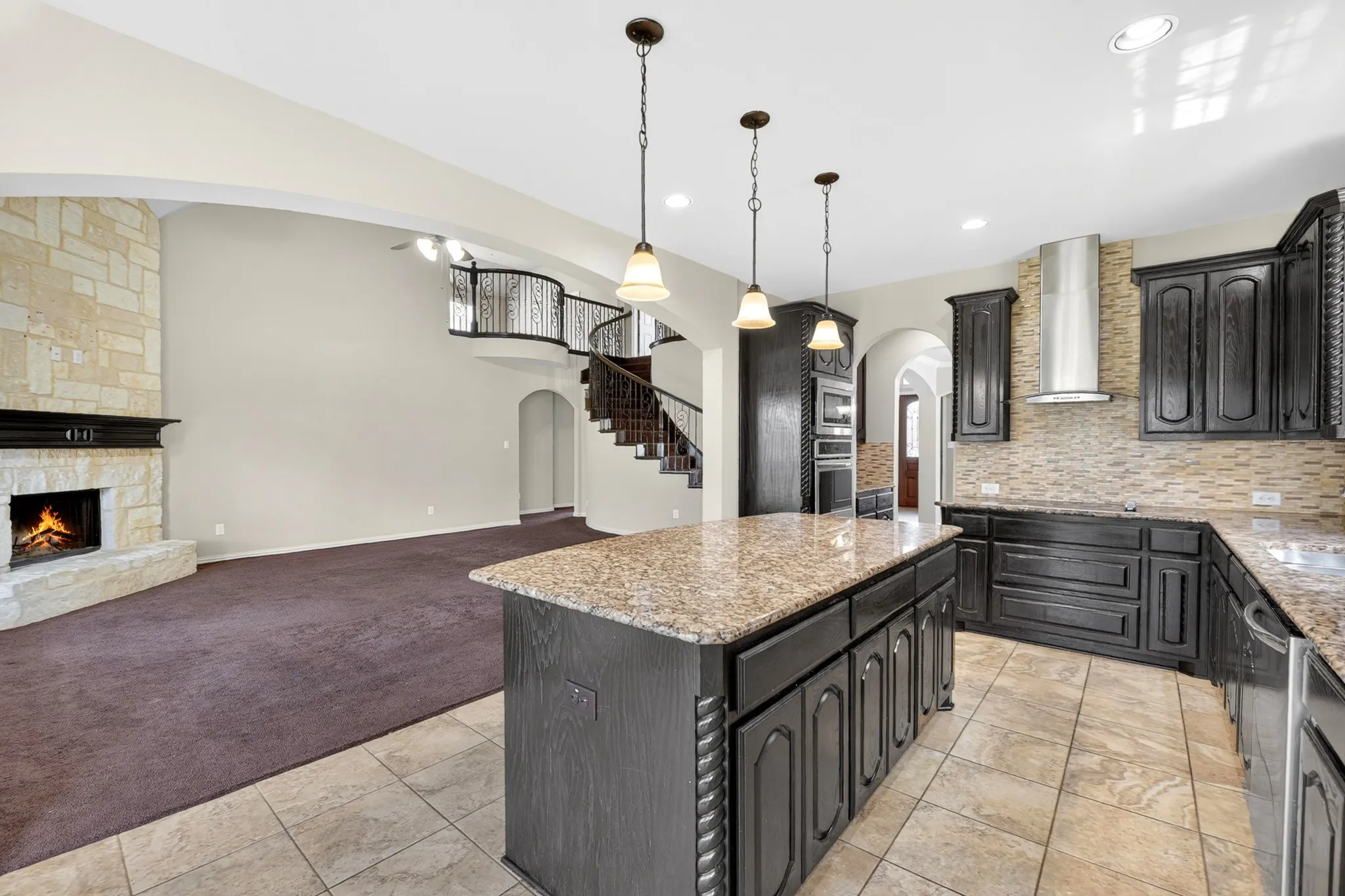 The open concept living area features a stone fireplace with a dark mantel, a curved staircase with a decorative railing, and recessed lighting