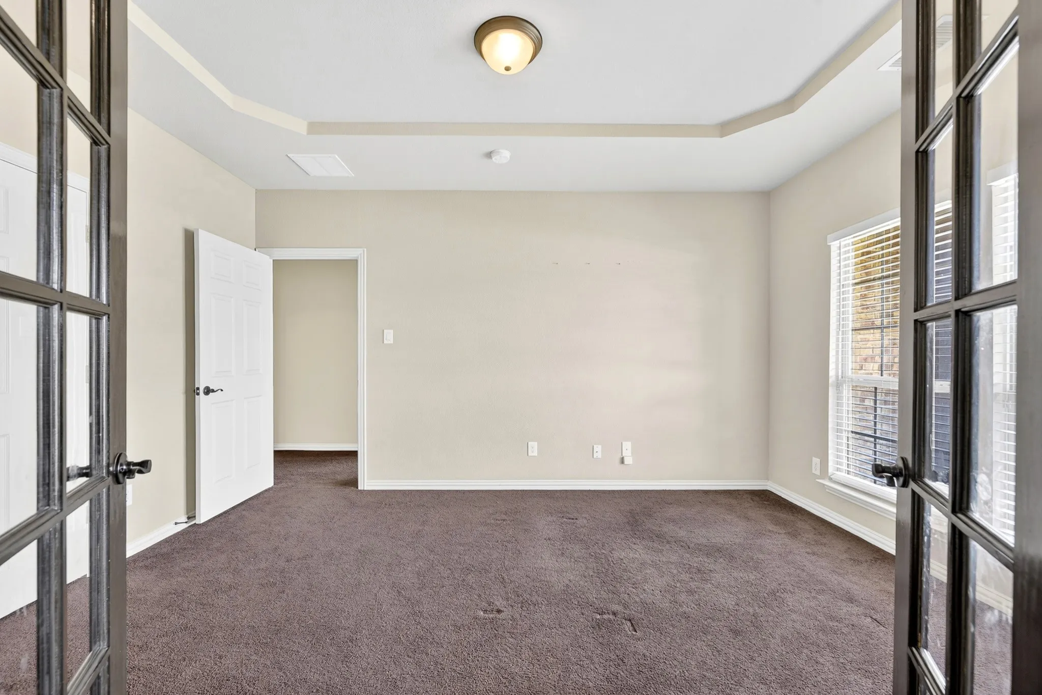 This room features a tray ceiling, plush carpet flooring, and a window with blinds