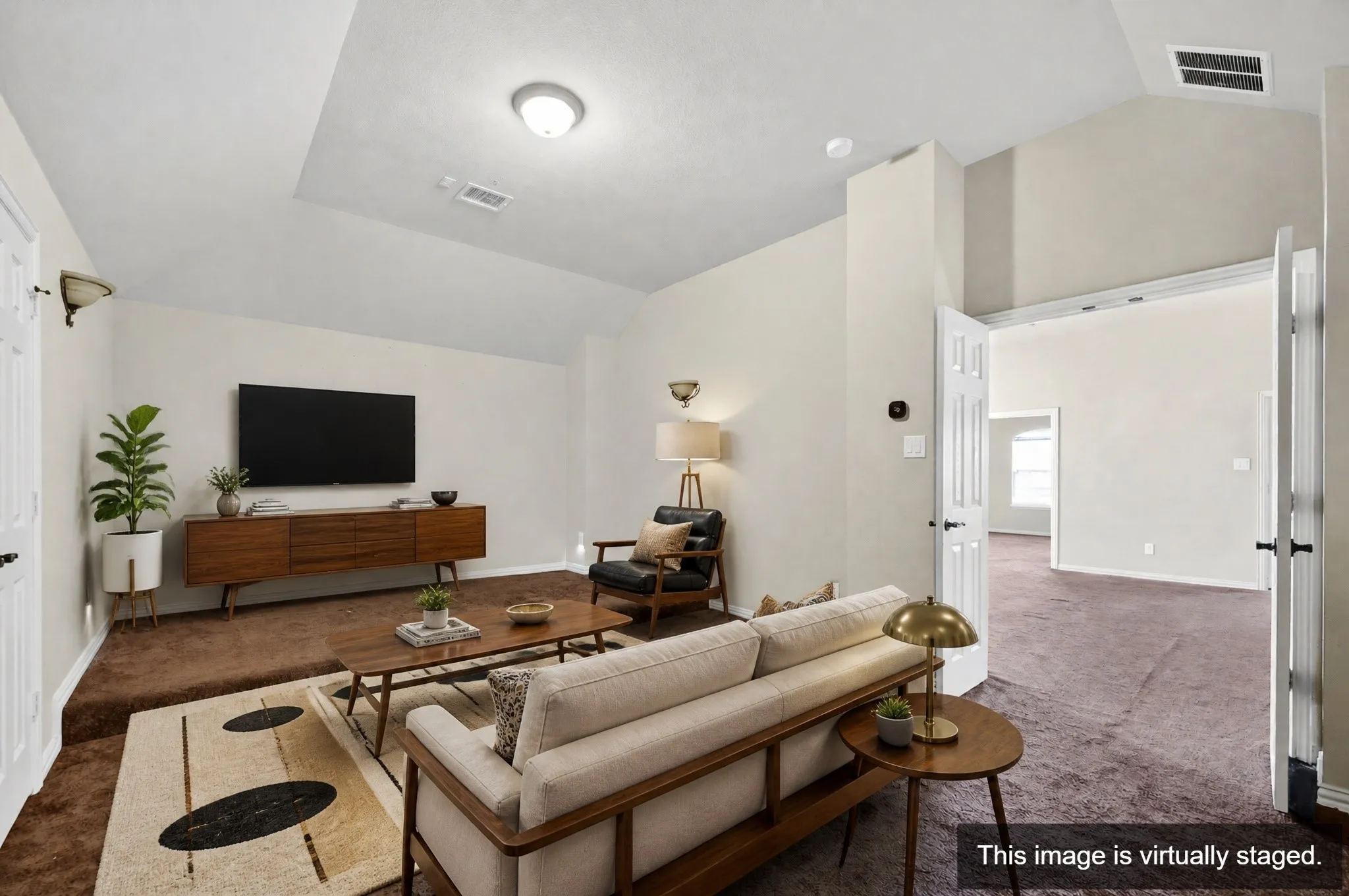 Living area featuring vaulted ceilings, wall-mounted light fixtures, a wide doorway, and carpet flooring