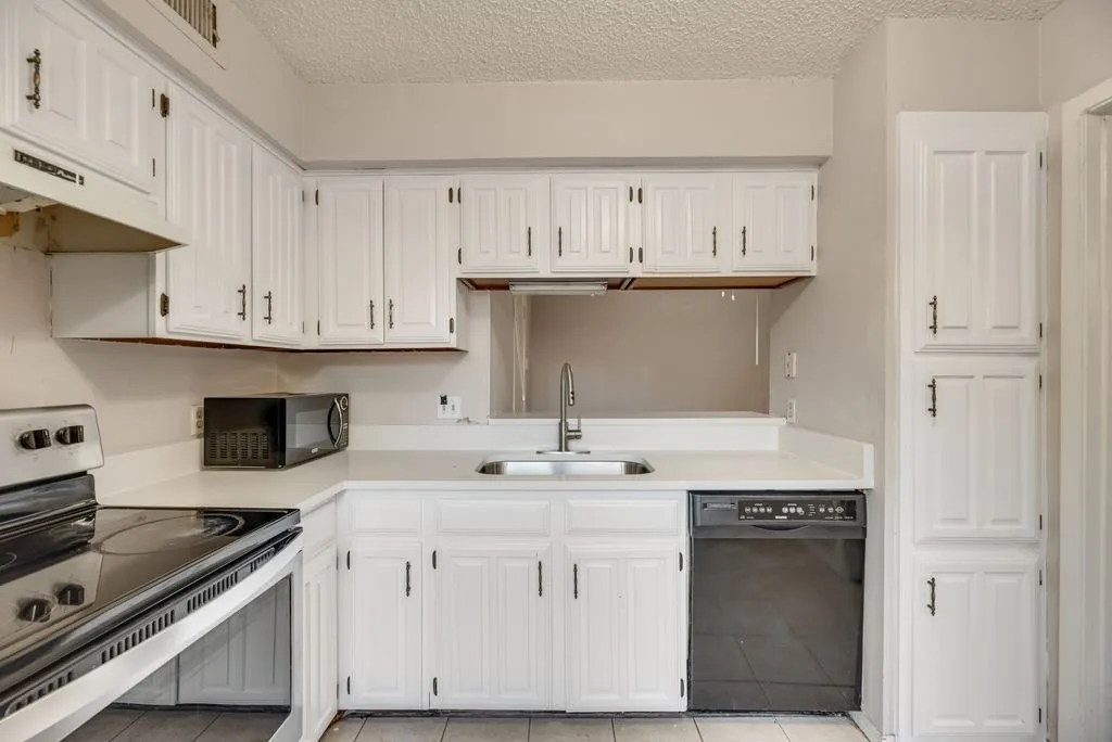 Kitchen featuring black appliances, a textured ceiling, white cabinetry, light countertops, and light tile patterned floors