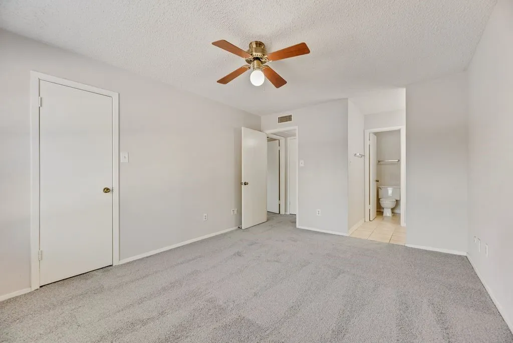 Unfurnished bedroom with carpet flooring, a textured ceiling, ensuite bathroom, and a ceiling fan