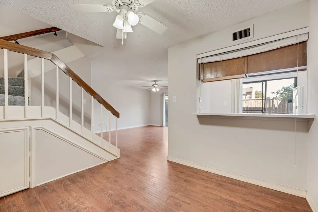 Unfurnished living room featuring ceiling fan, wood finished floors, a textured ceiling, and stairs