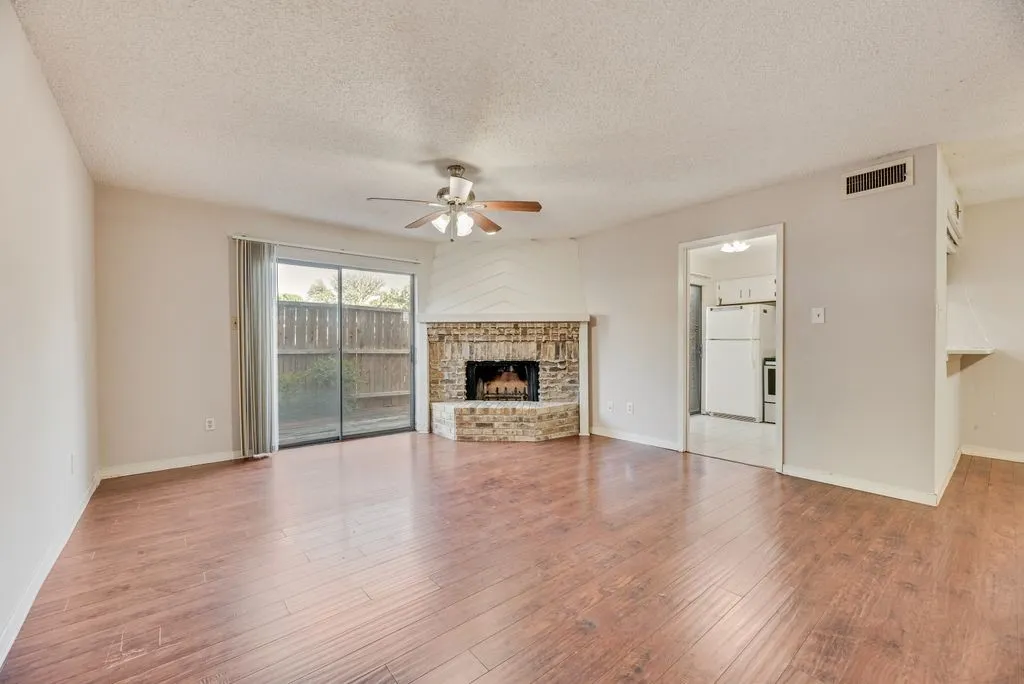 Unfurnished living room featuring ceiling fan, a textured ceiling, wood finished floors, and a fireplace