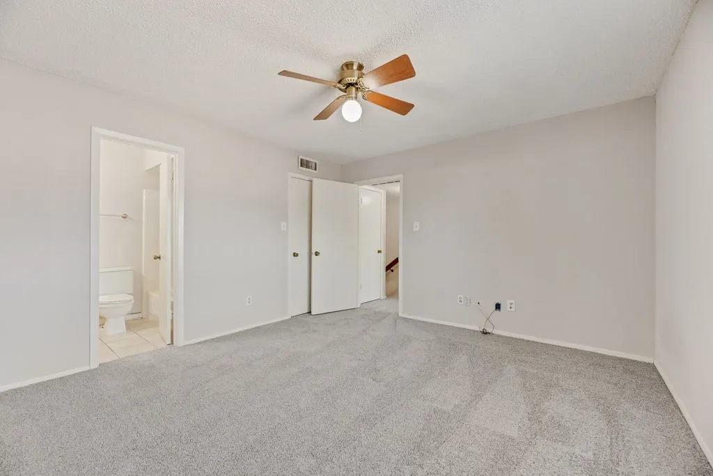Unfurnished bedroom featuring light colored carpet, connected bathroom, a textured ceiling, and ceiling fan