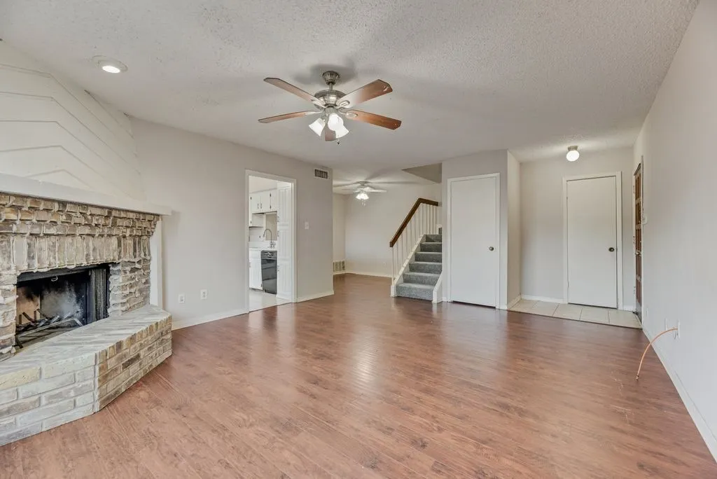 Unfurnished living room featuring a brick fireplace, a ceiling fan, stairs, a textured ceiling, and wood finished floors