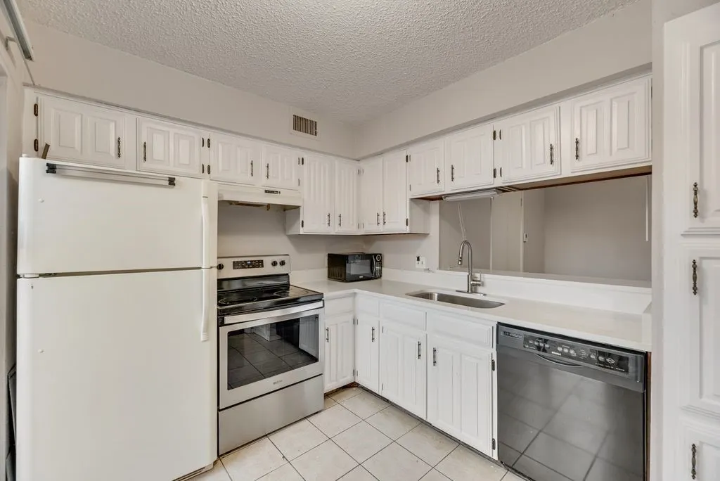Kitchen with black appliances, light countertops, white cabinetry, light tile patterned floors, and a textured ceiling