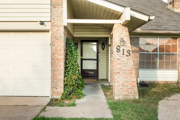View of exterior entry with a garage, roof with shingles, and brick siding