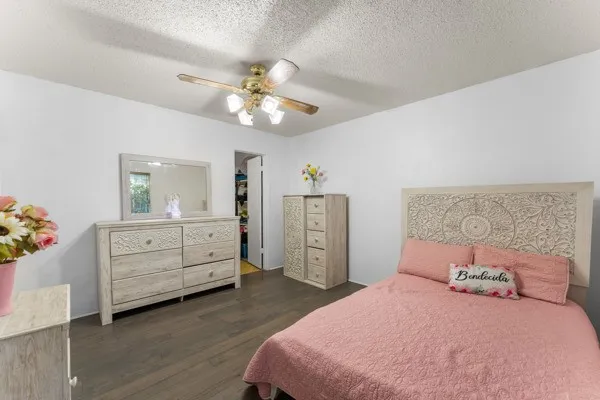 Bedroom featuring dark wood-style flooring, a textured ceiling, ceiling fan, and a spacious closet